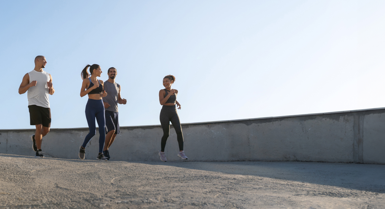 Four people are jogging together on a paved path against a clear blue sky.