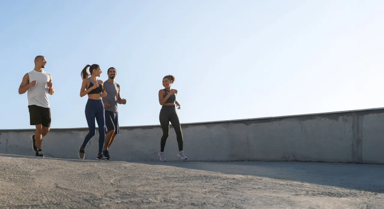 Four people are jogging together on a paved path against a clear blue sky.