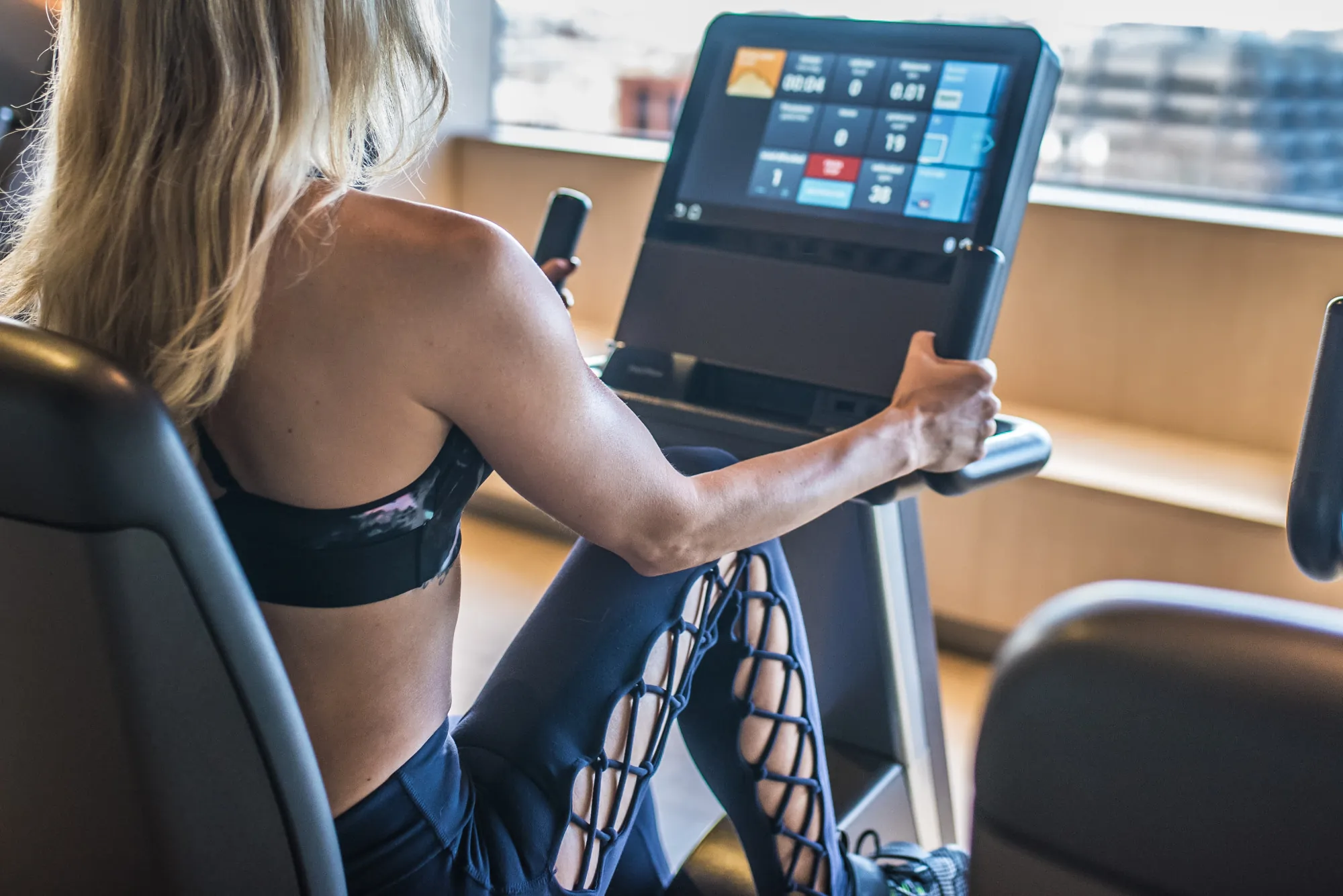 Eine Frau trainiert auf einem Bein-Ergometer in einem Fitnessstudio mit modernen Trainingsdaten auf dem Bildschirm.