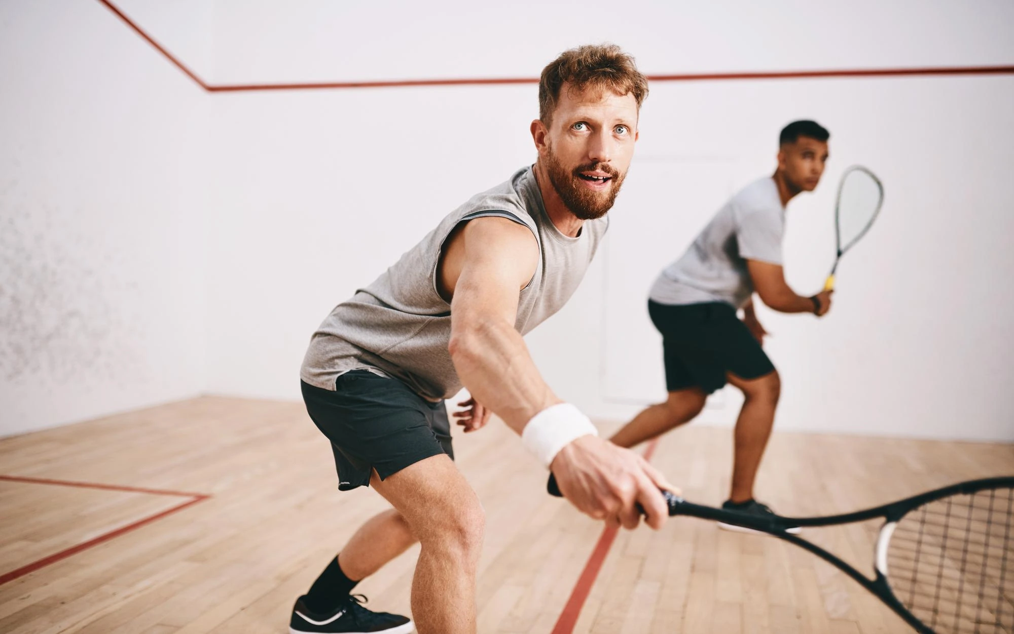 Zwei Männer spielen Squash in einem Squash-Court, einer bereitet einen Schlag vor.