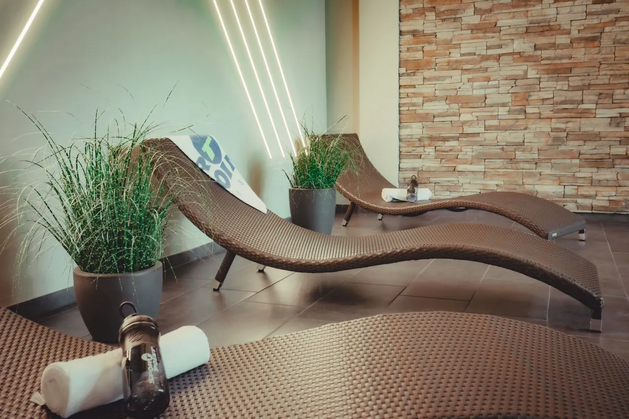 Moderne braune Liegestühle in einem Wellnessbereich mit grünen Pflanzen und Wandbeleuchtung.