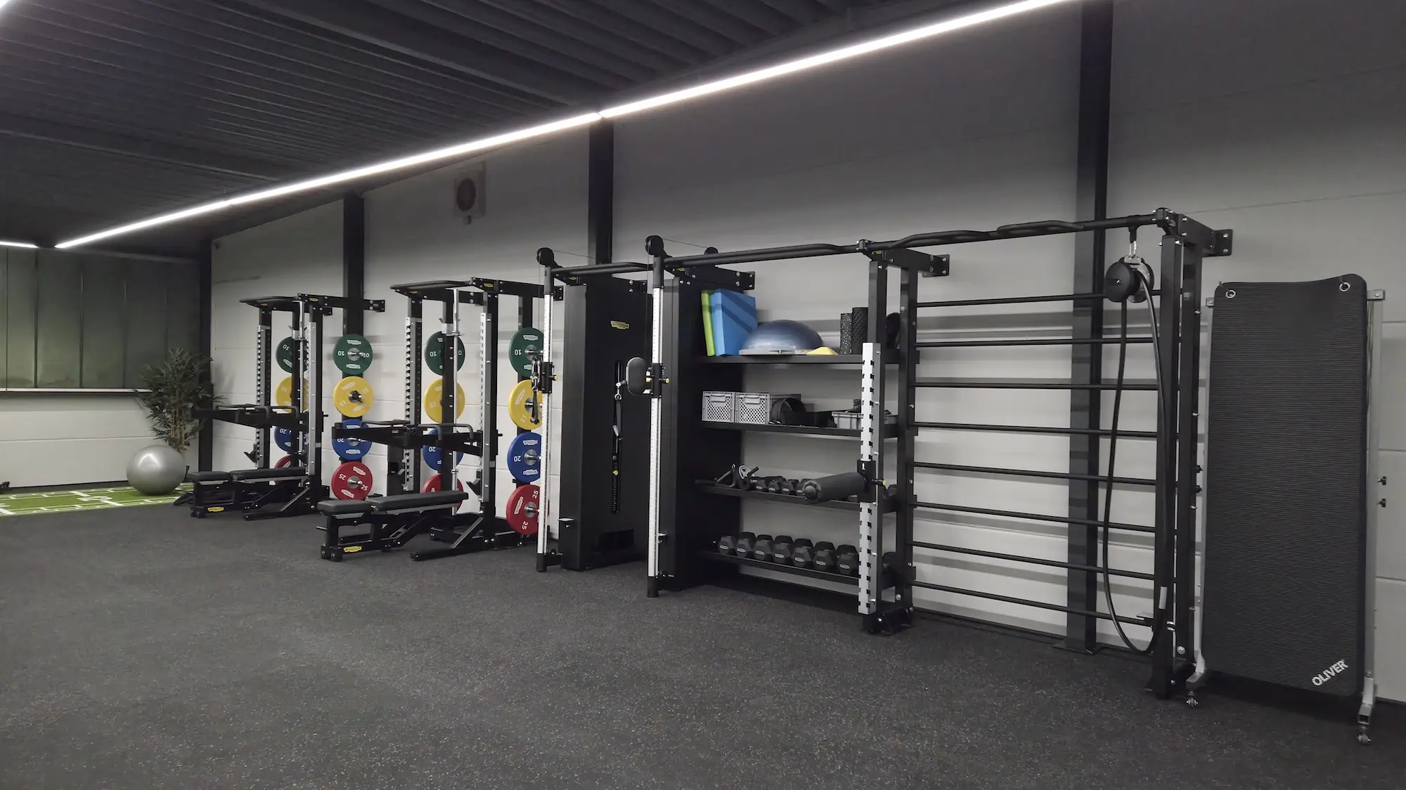 Fitnessraum mit Hanteln, Gewichtsscheiben, Fitnessmatten und Trainingsgeräten an einer Wand.