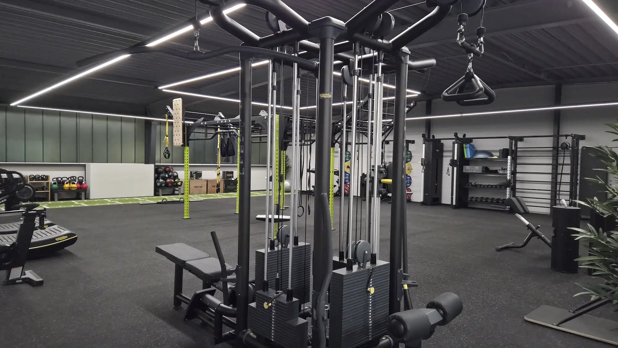 Moderner Fitnessraum mit Krafttrainingsgeräten, verstellbarer Bank und Hantelregalen in einem gut beleuchteten Raum.