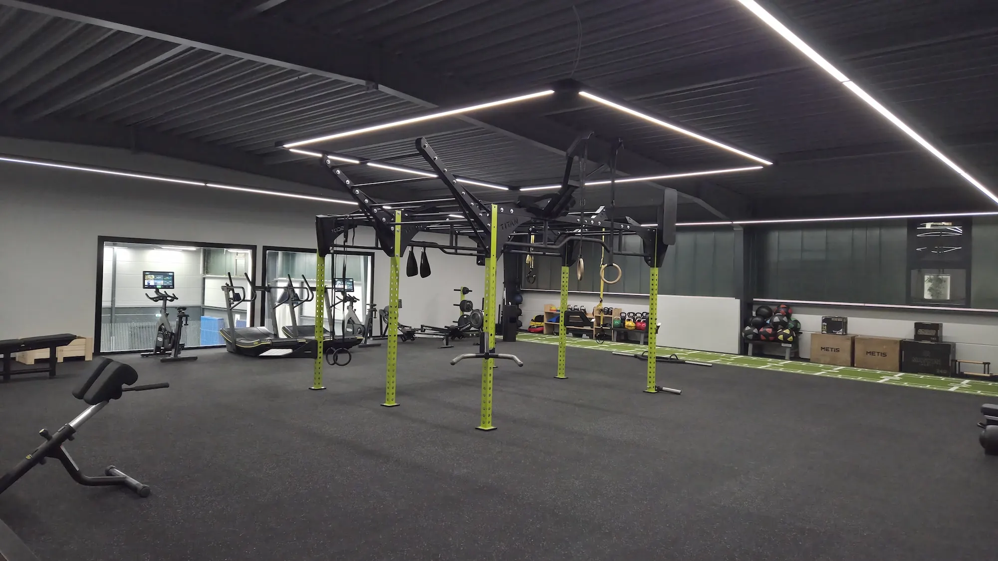 Geräumiger Fitnessraum mit funktionalem Trainingsgerät in der Mitte, Laufbändern, Fahrradergometern und Kettlebells.