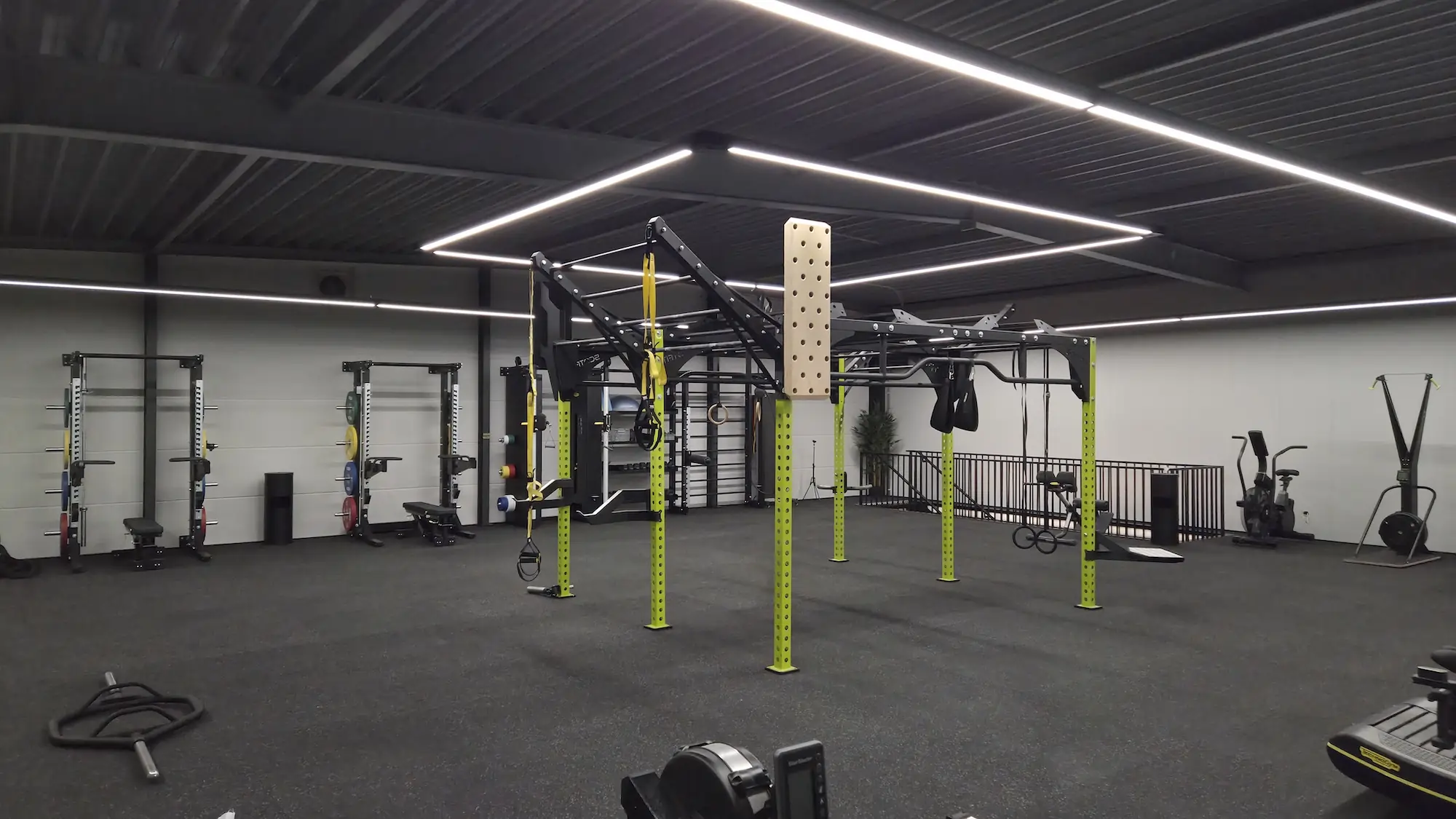 Großer moderner Fitnessraum mit multifunktionaler Trainingsstation in der Mitte und Gewichten an der Wand.