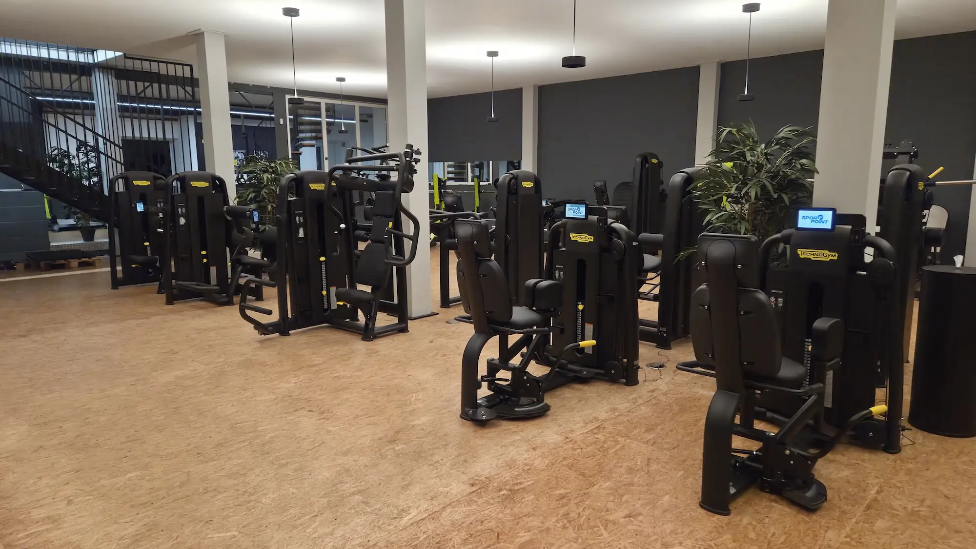 Moderne Fitnessgeräte in einem hell erleuchteten Fitnessstudio mit Holzfußboden.