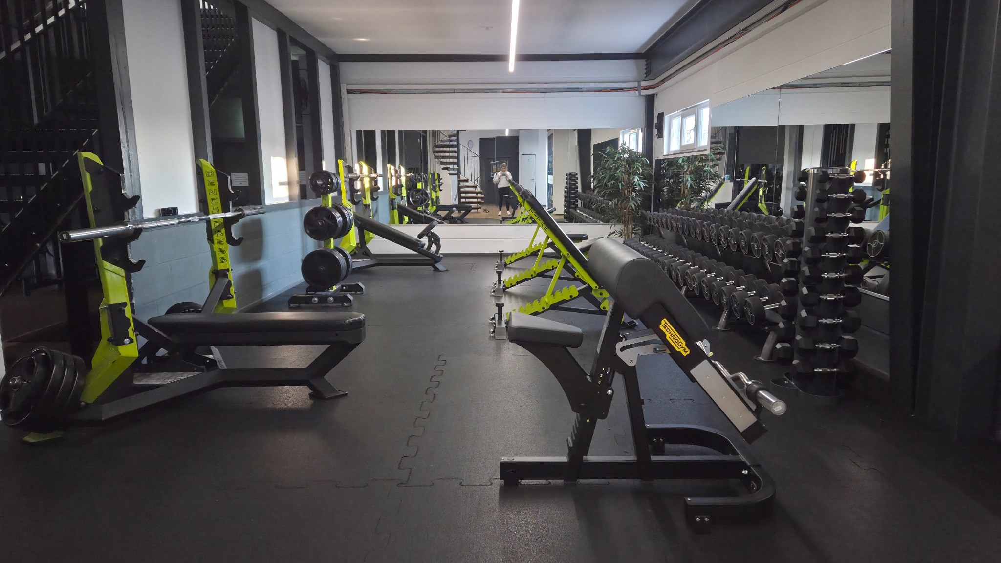 Fitnessstudio mit Hantelbänken, Kurzhanteln und Spiegelwand für Krafttraining.