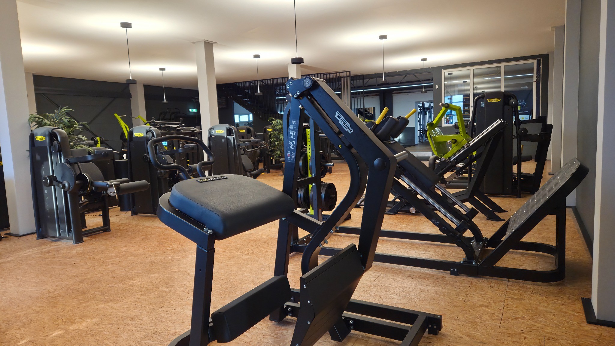Fitnessraum mit mehreren schwarzen und grünen Kraftgeräten auf Holzfußboden.