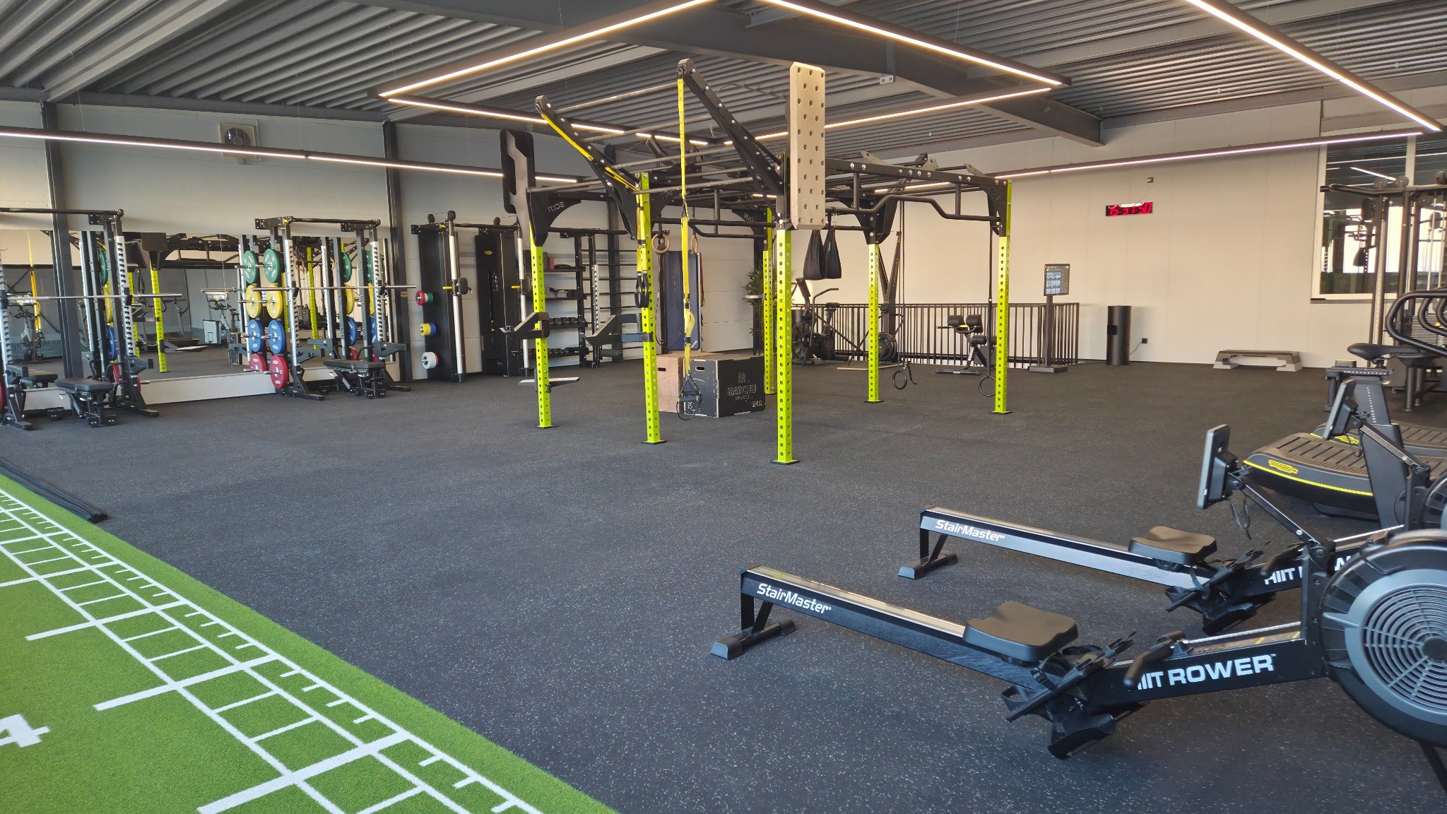 Moderner Fitnessraum mit Rudergeräten, Multistation, Spiegeln und Hantelständern auf kleinem Platz.