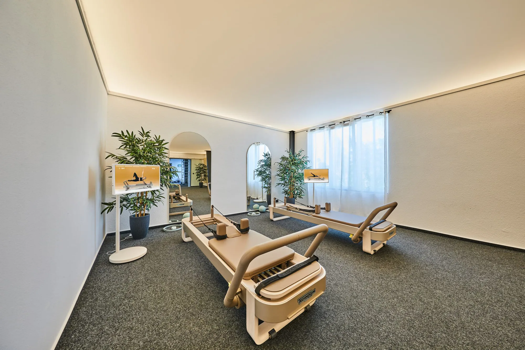 Reformer-Pilates-Raum im Sport Point Gießen mit zwei Technogym Reformern, Bildschirmen mit Workout-Anleitung und Pflanzen.
