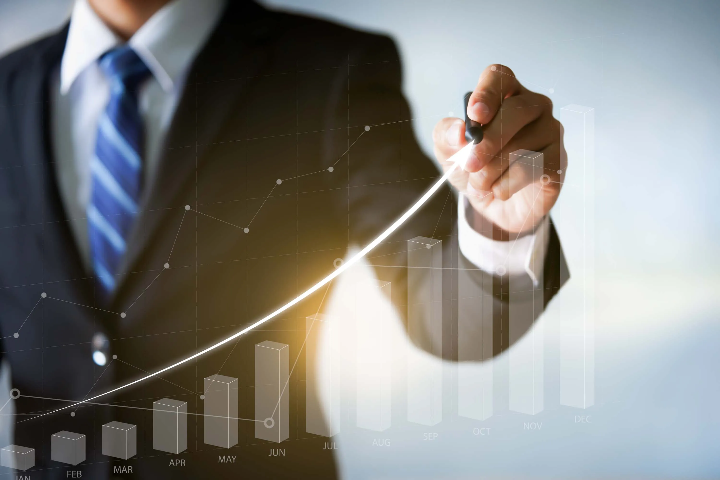 Businessman in a suit drawing an upward arrow on a virtual bar chart representing growth over the months of the year.