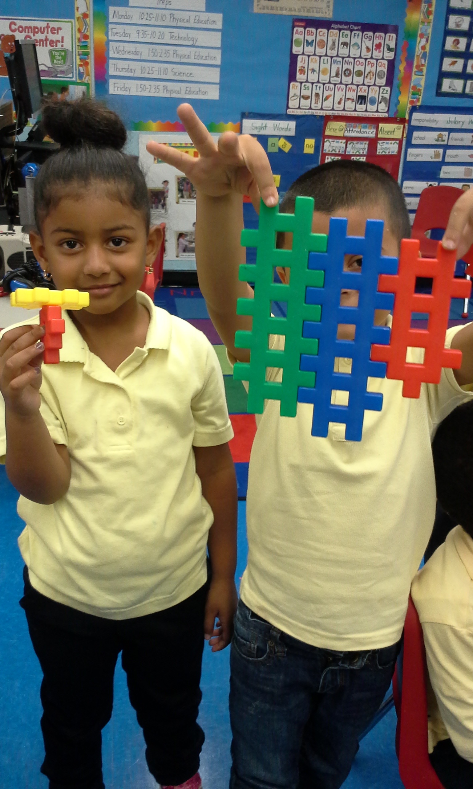 Two students holding colorful interlocking plastic building blocks in classroom