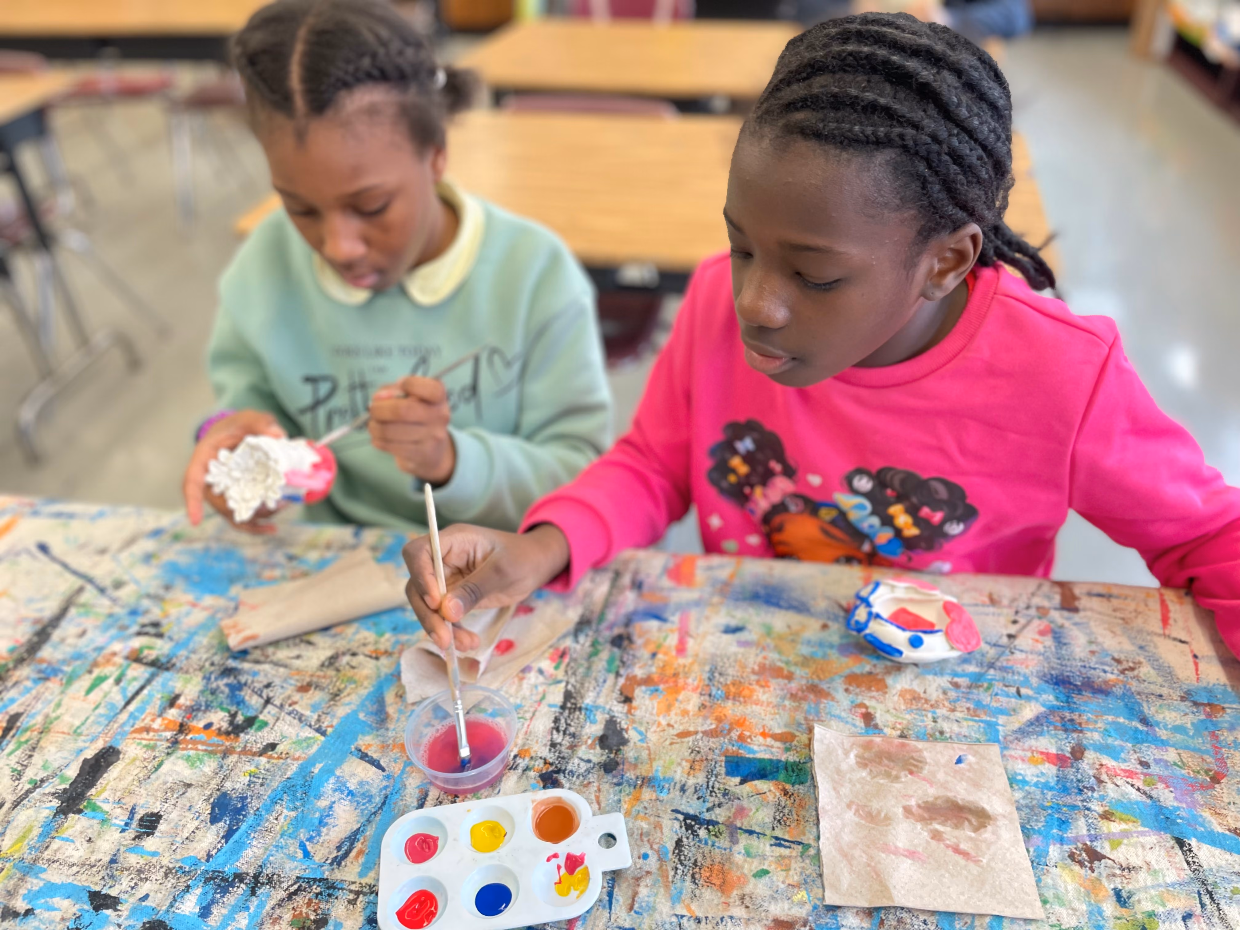 Two students painting clay sculptures during art class