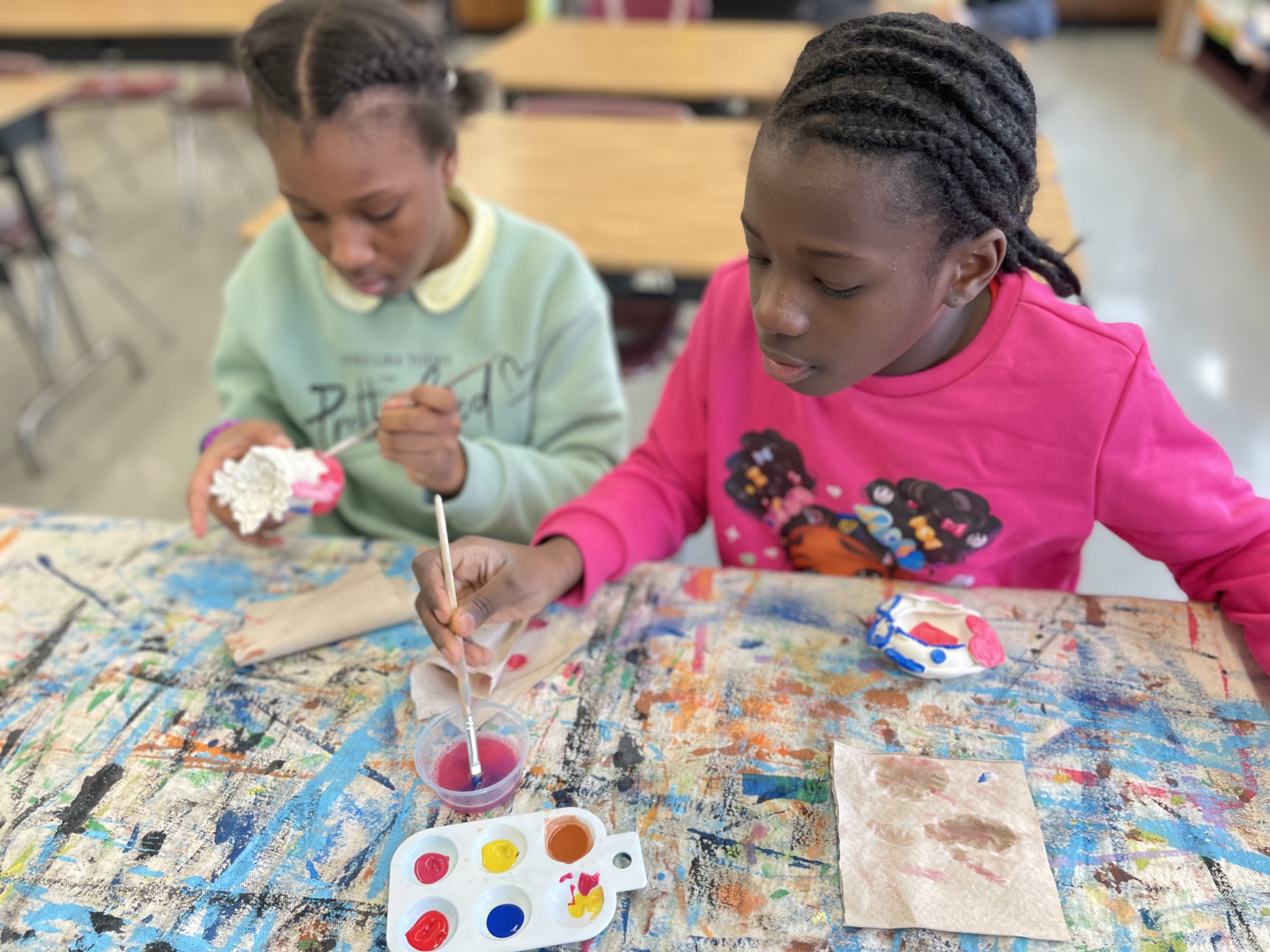 Two students painting clay sculptures during art class