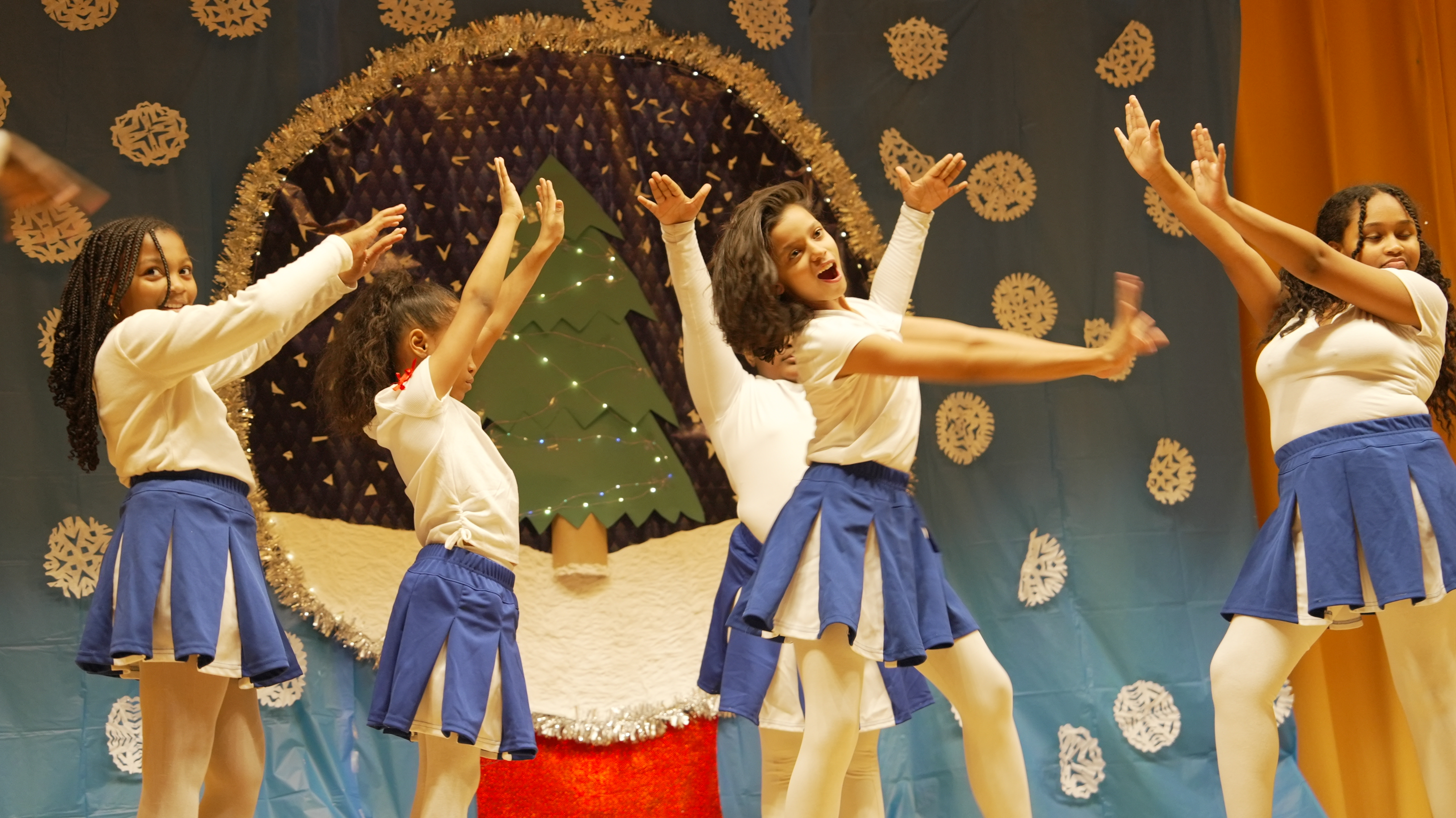 Students performing a holiday dance on stage in uniform
