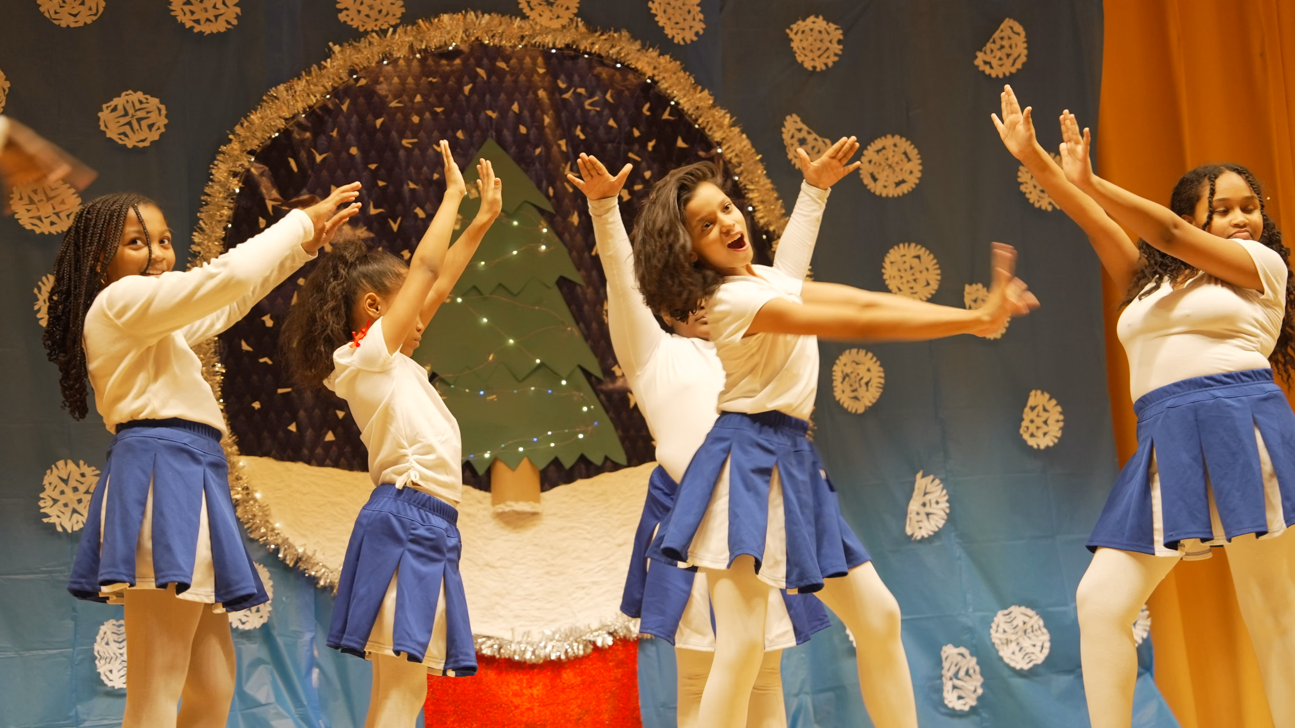 Students performing a holiday dance on stage in uniform