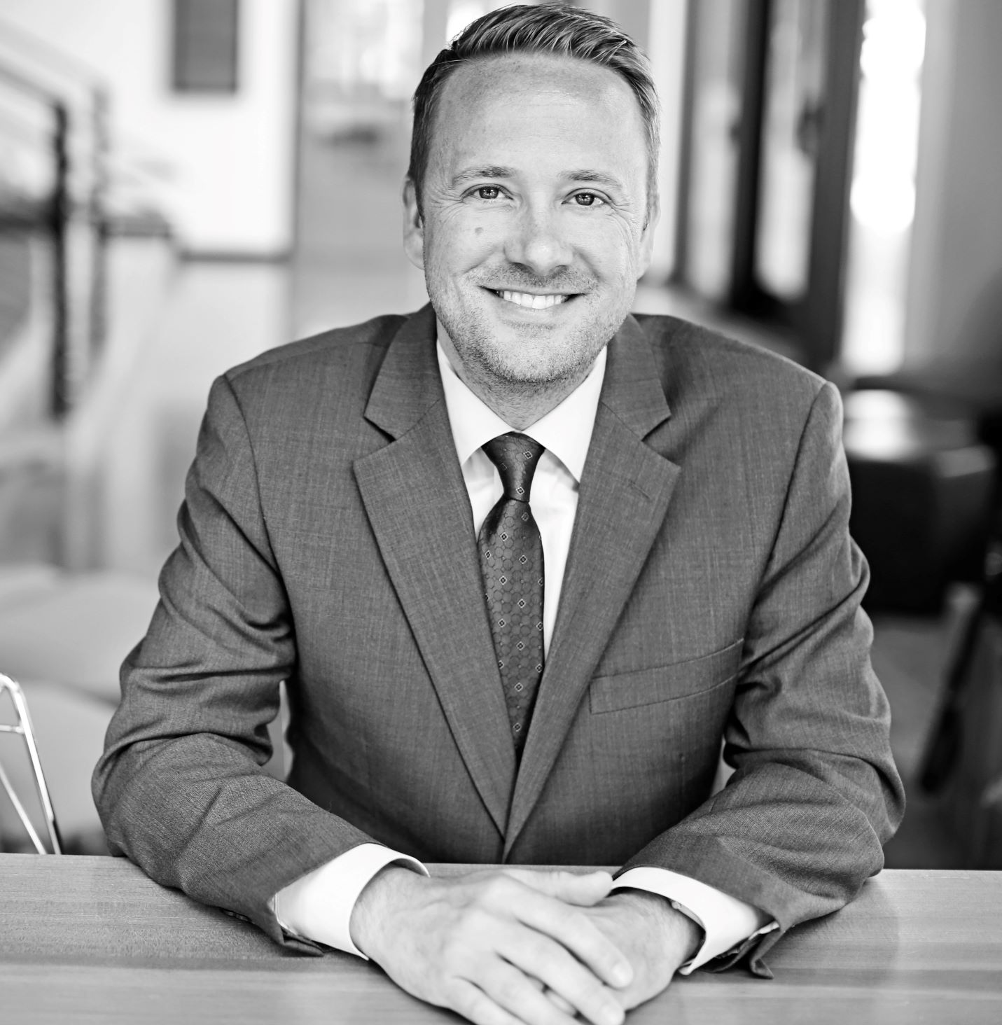 black and white image of man in suit and tie sitting at table with hands crossed