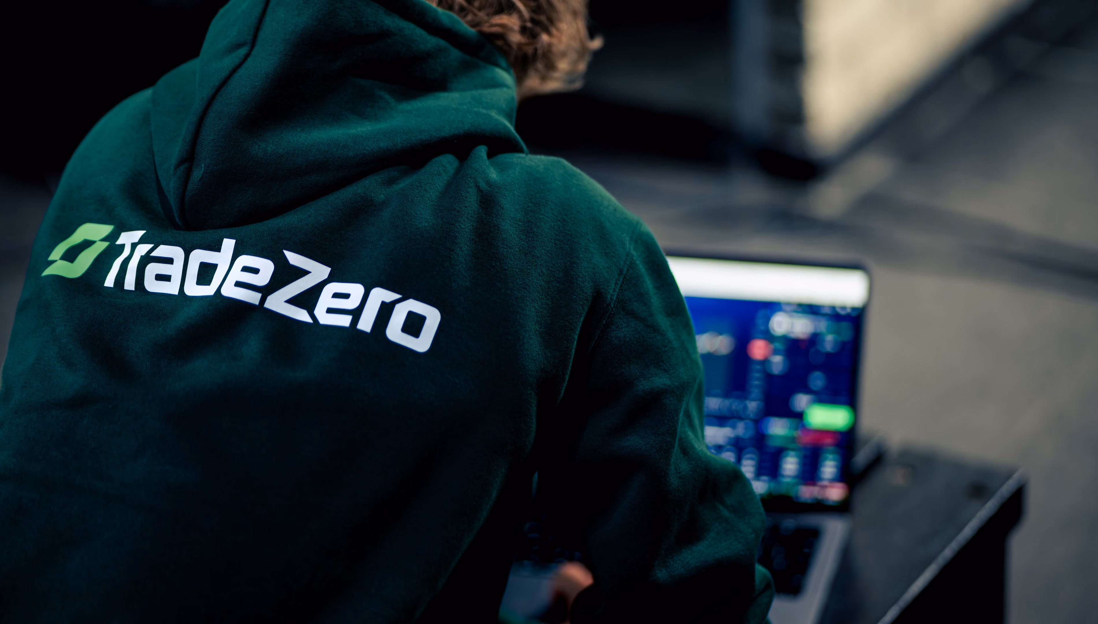 Persoon met een groene hoodie met TradeZero-logo op de rug werkt op een laptop met financiële data.