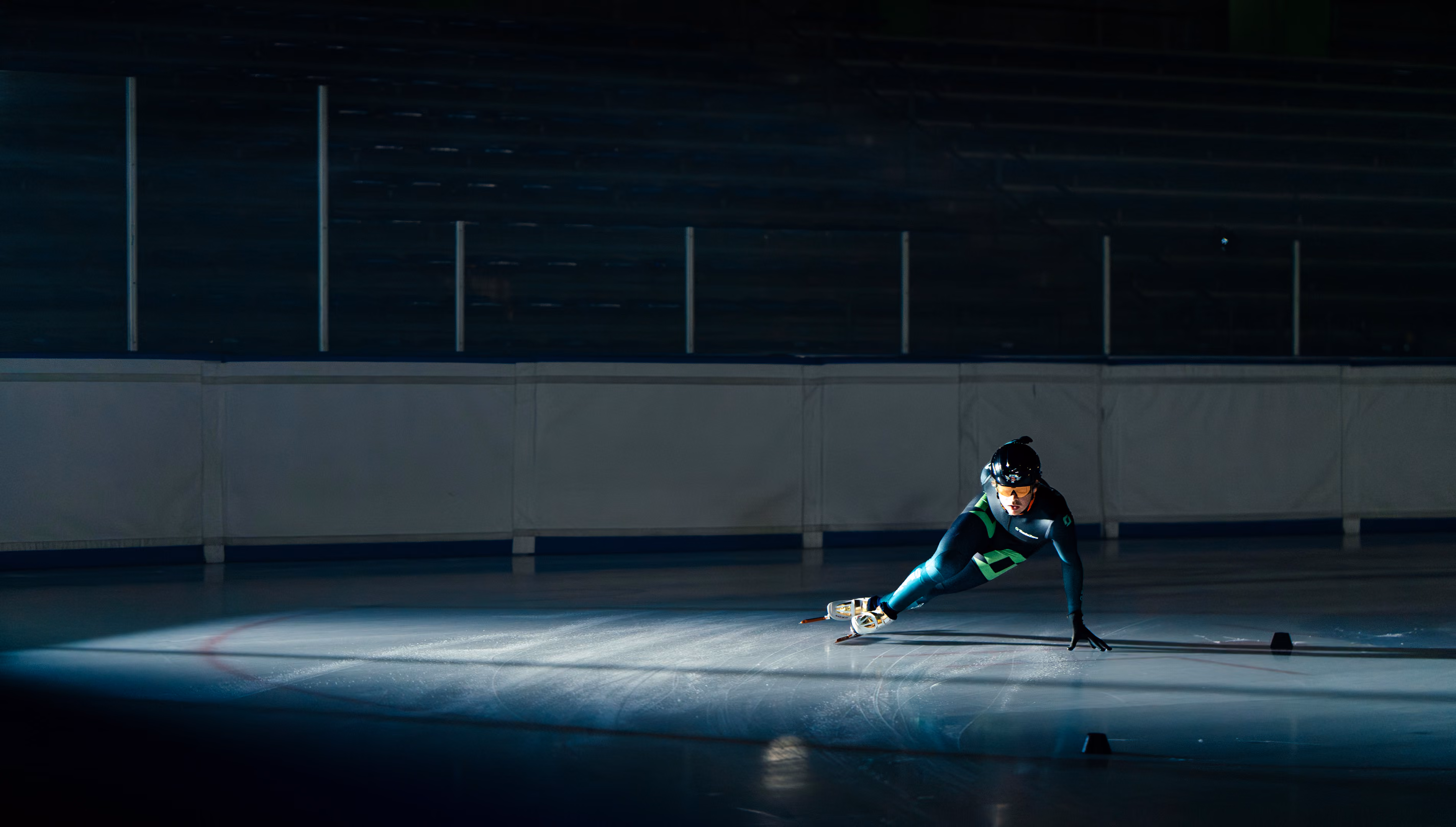 Schaatser in een donker ijsstadion glijdt laag over het ijs met één hand op de grond.