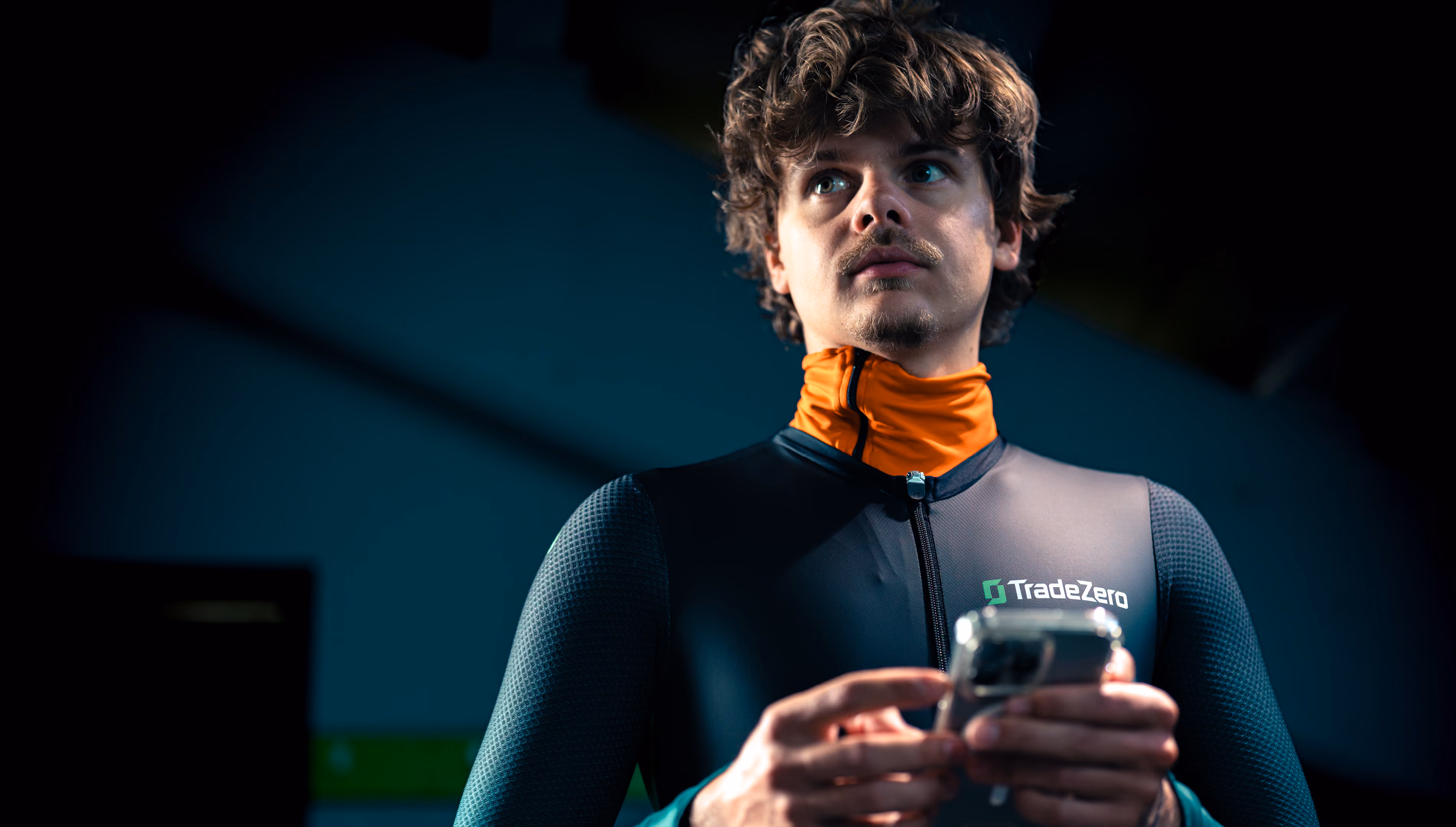 Man wearing a TradeZero jacket looking away while holding a smartphone with both hands.