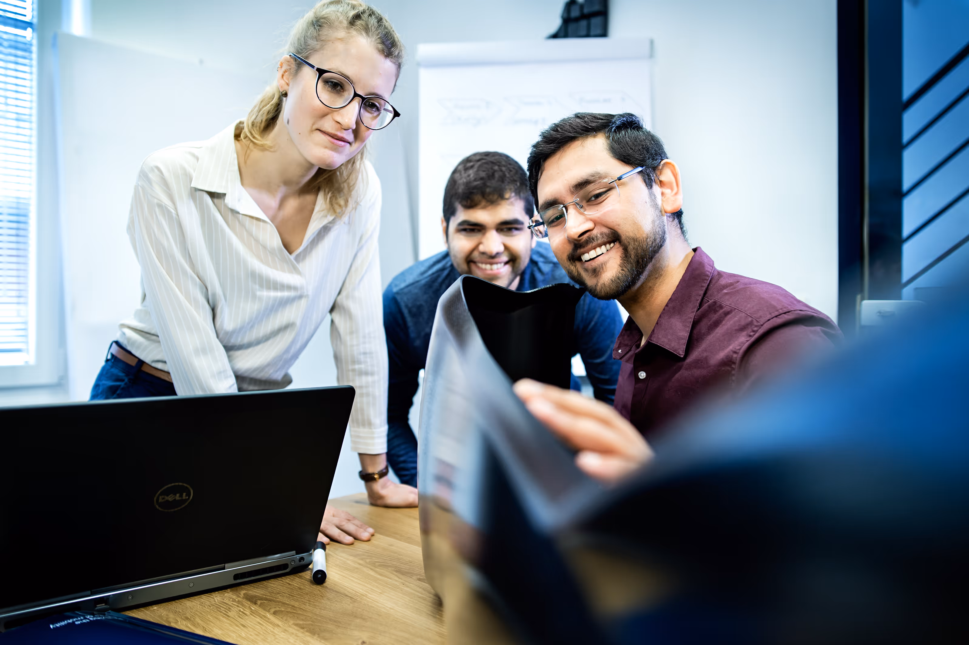 A woman and two men are looking at a laptop.