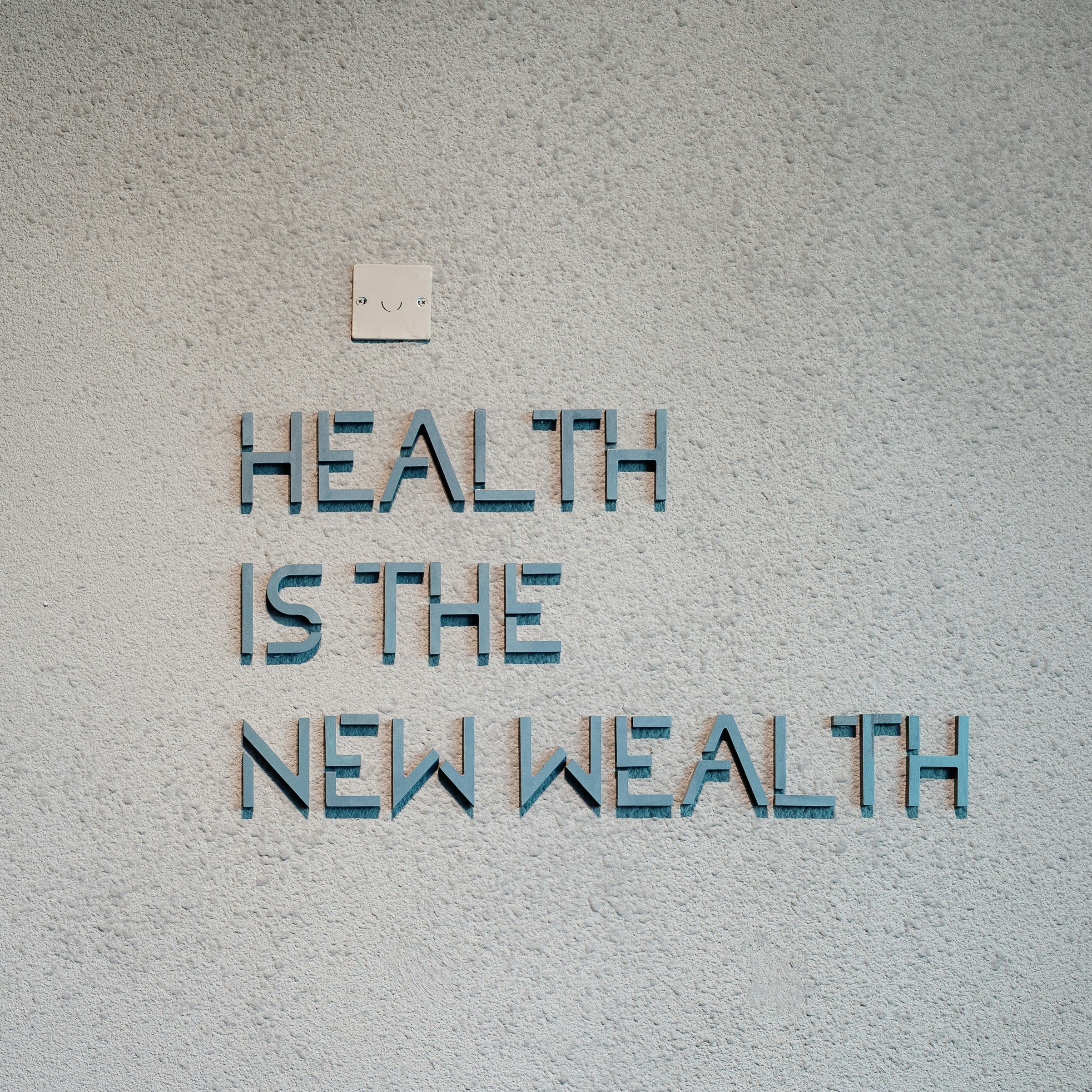 Tekst op een grijze muur met de woorden 'HEALTH IS THE NEW WEALTH' in blauwe letters.