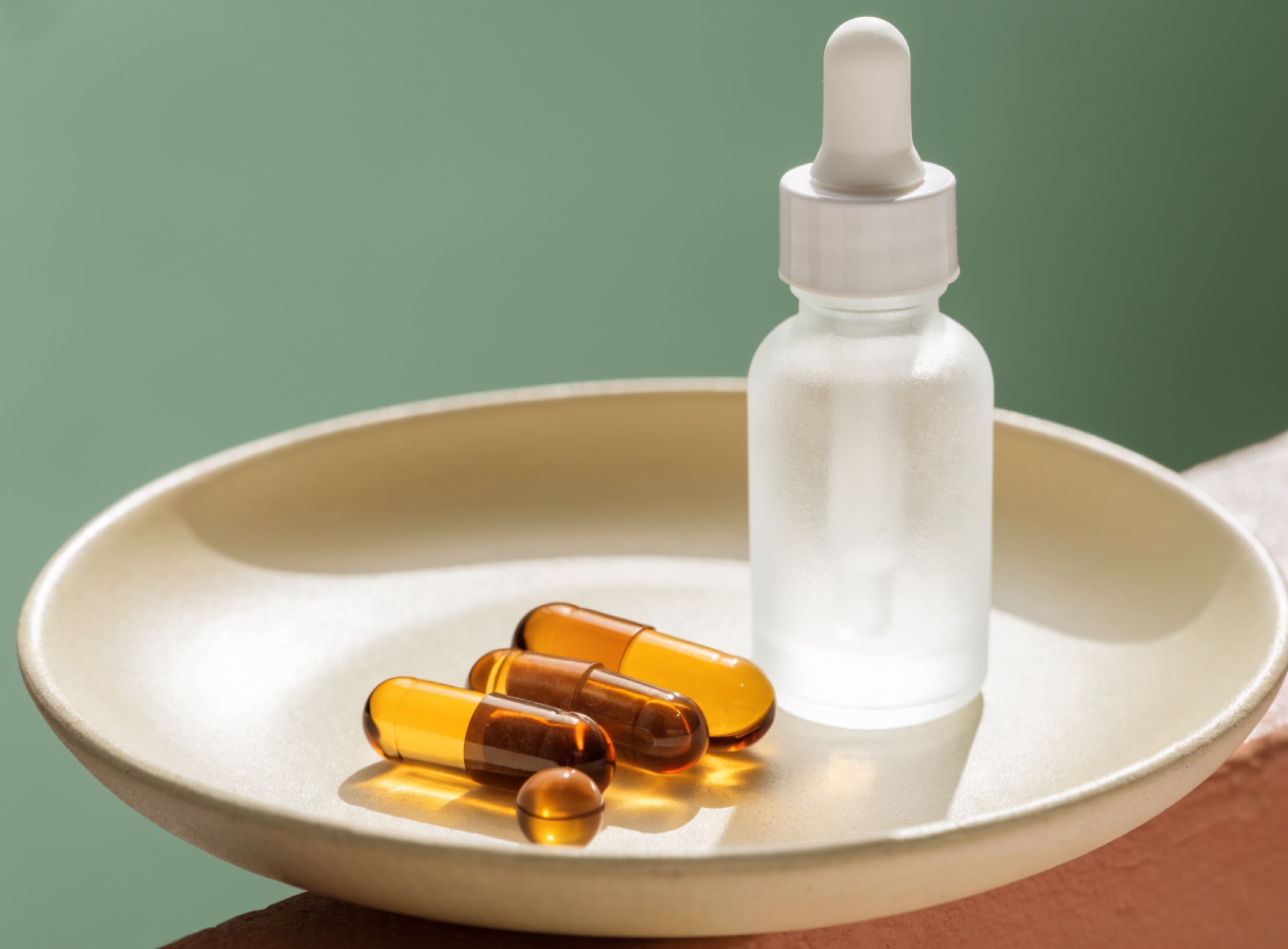 Capsules en een mat glazen druppelflesje op een schaaltje, stilleven