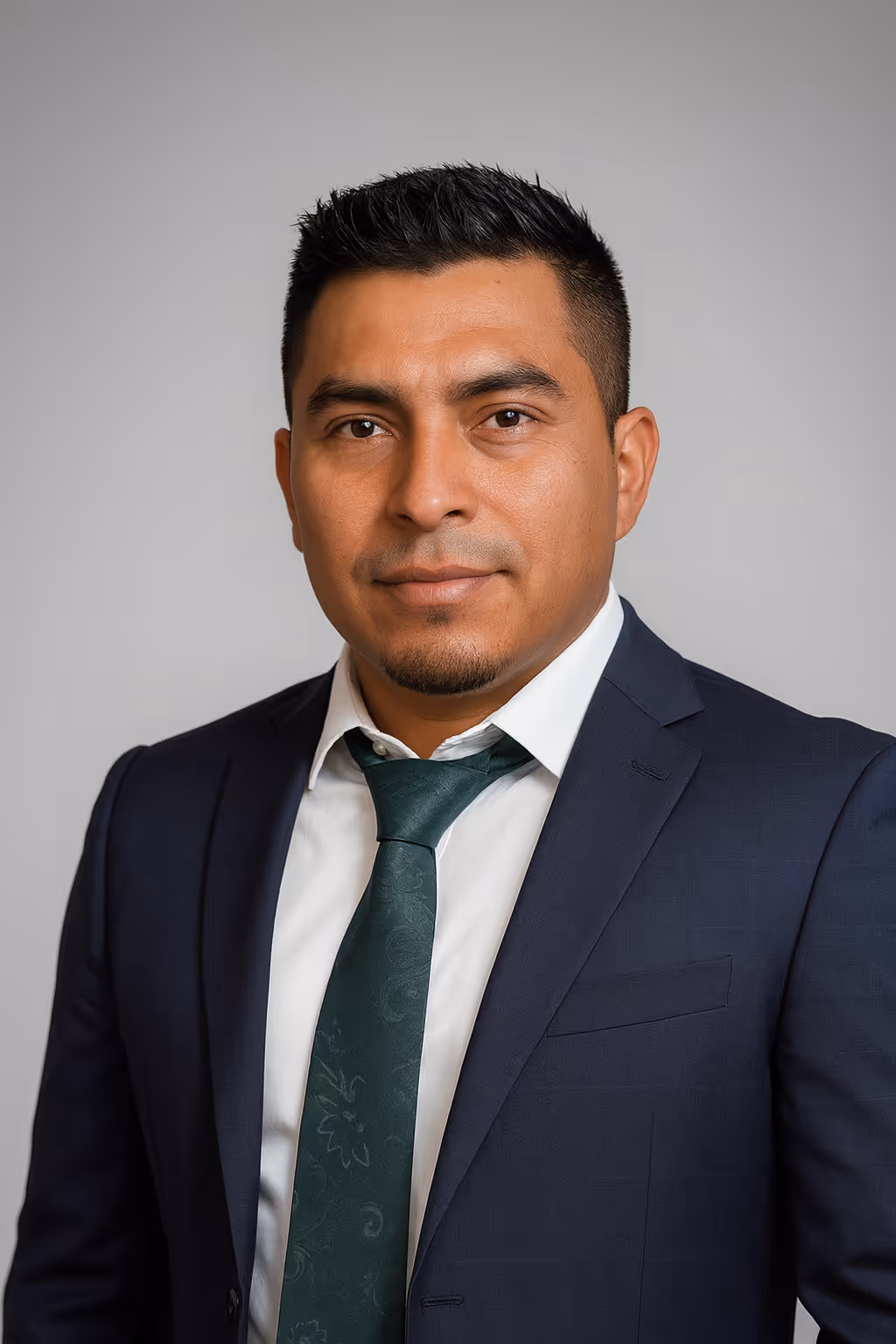 Omar posing for a headshot wearing a dark blue suit with a white-collar shirt and emerald green tie. 