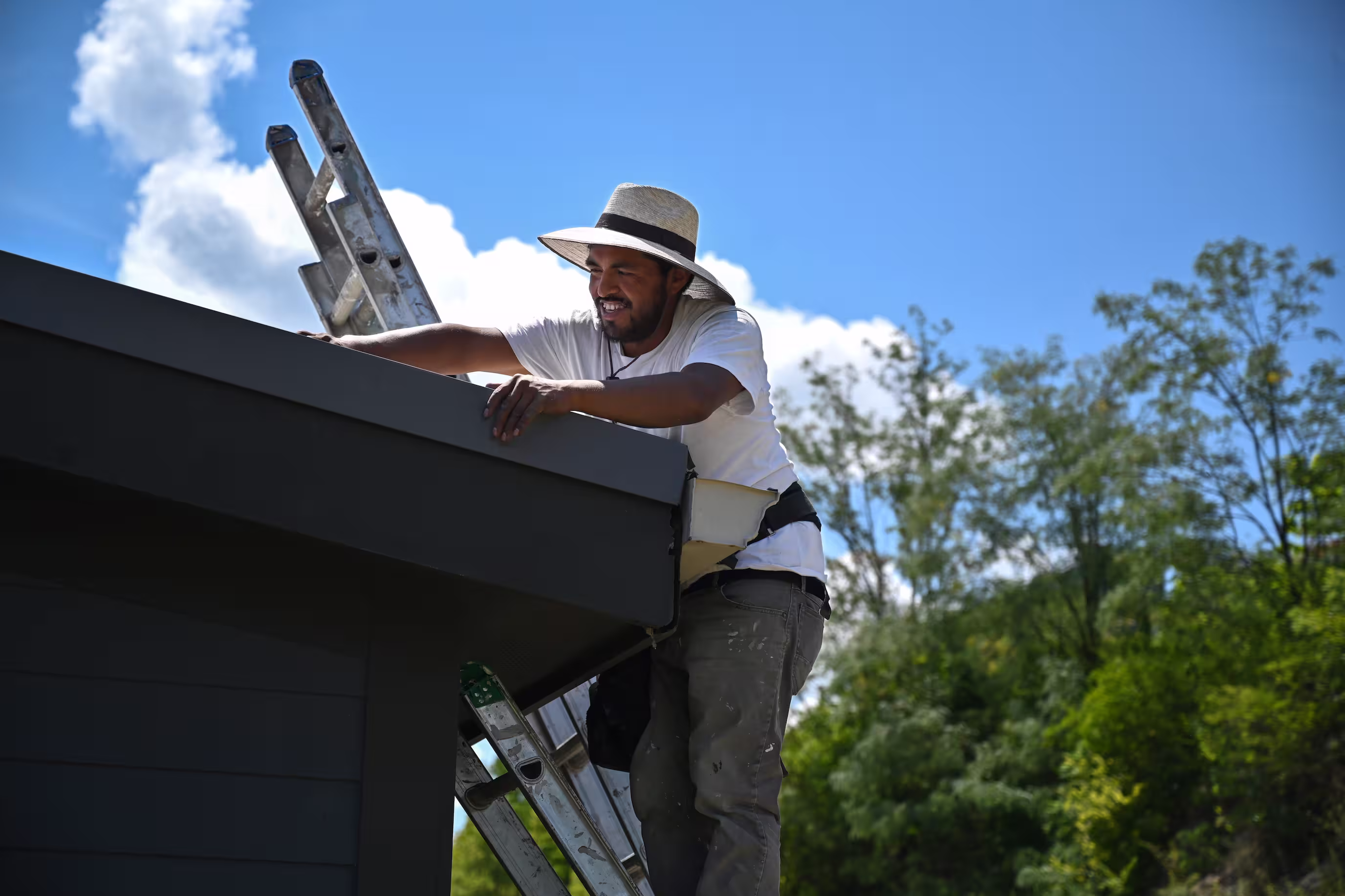 Contractor on a ladder completing finishing touches to newly installed roofing shingles on a residential property.