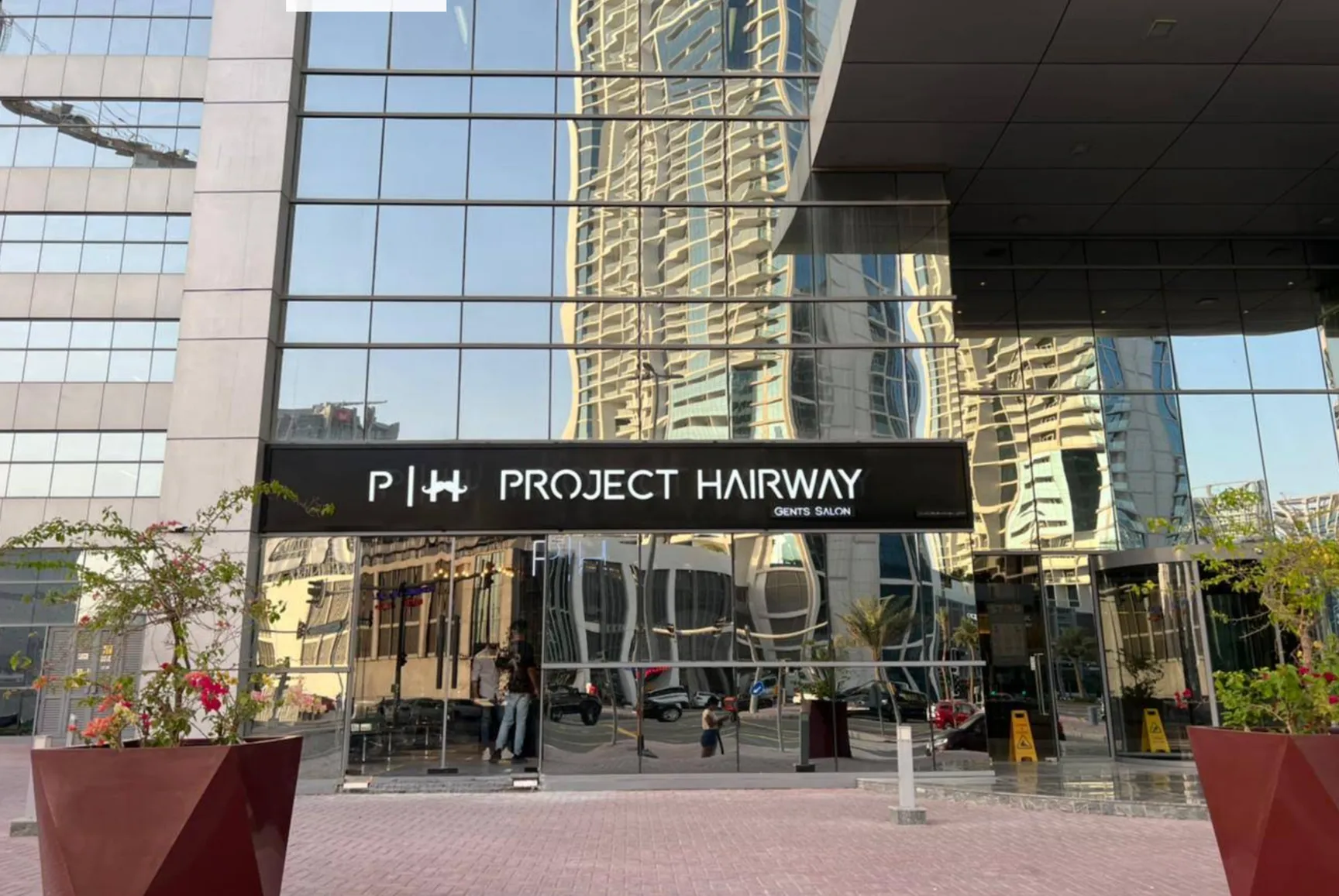 Project Hairway storefront exterior in modern Dubai business district with glass facade, premium gents salon signage, business bay area