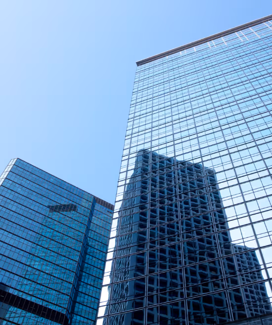 Two modern glass skyscrapers with blue-tinted windows reflecting each other against a clear sky.