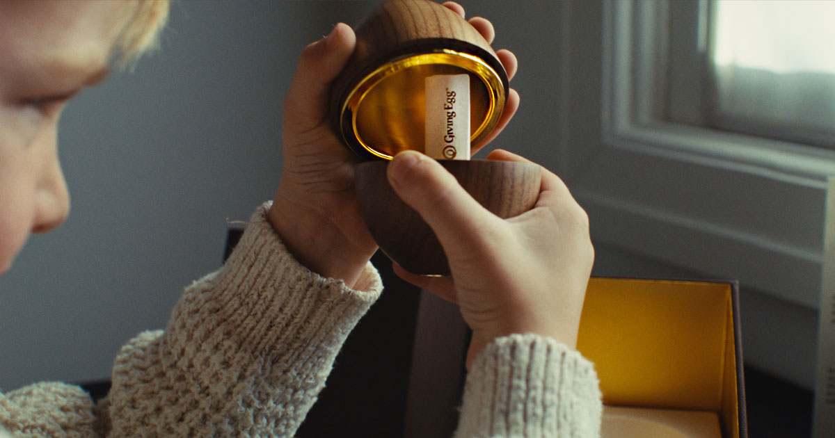 “Child holding and opening a handcrafted wooden keepsake container with a polished gold interior near a window in soft natural light.”