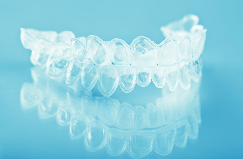 A close-up shot of a clear orthodontic clear aligner resting on a reflective blue surface. — Clio Dental Studio