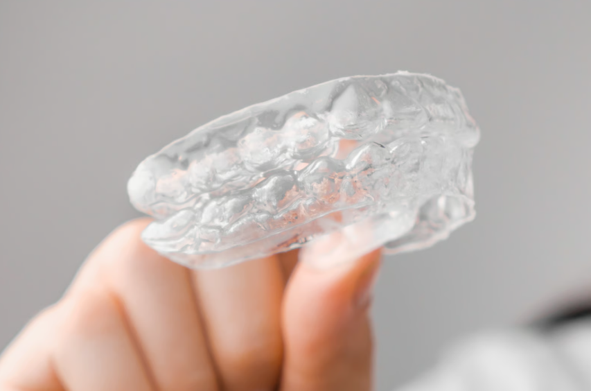 A person is holding up a clear dental aligner against a neutral gray background. — Clio Dental Studio