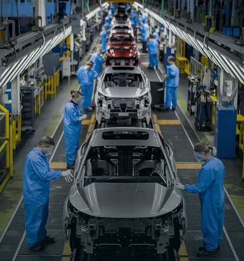 Trabajadores con equipo azul ensamblan autos en una línea de producción en fábrica automotriz.