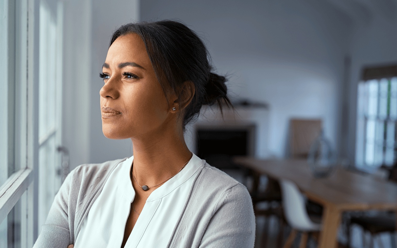 Woman thoughtfully looking out a window while contemplating hysterectomy options, highlighting care from the best gynecological surgeon in Los Angeles.