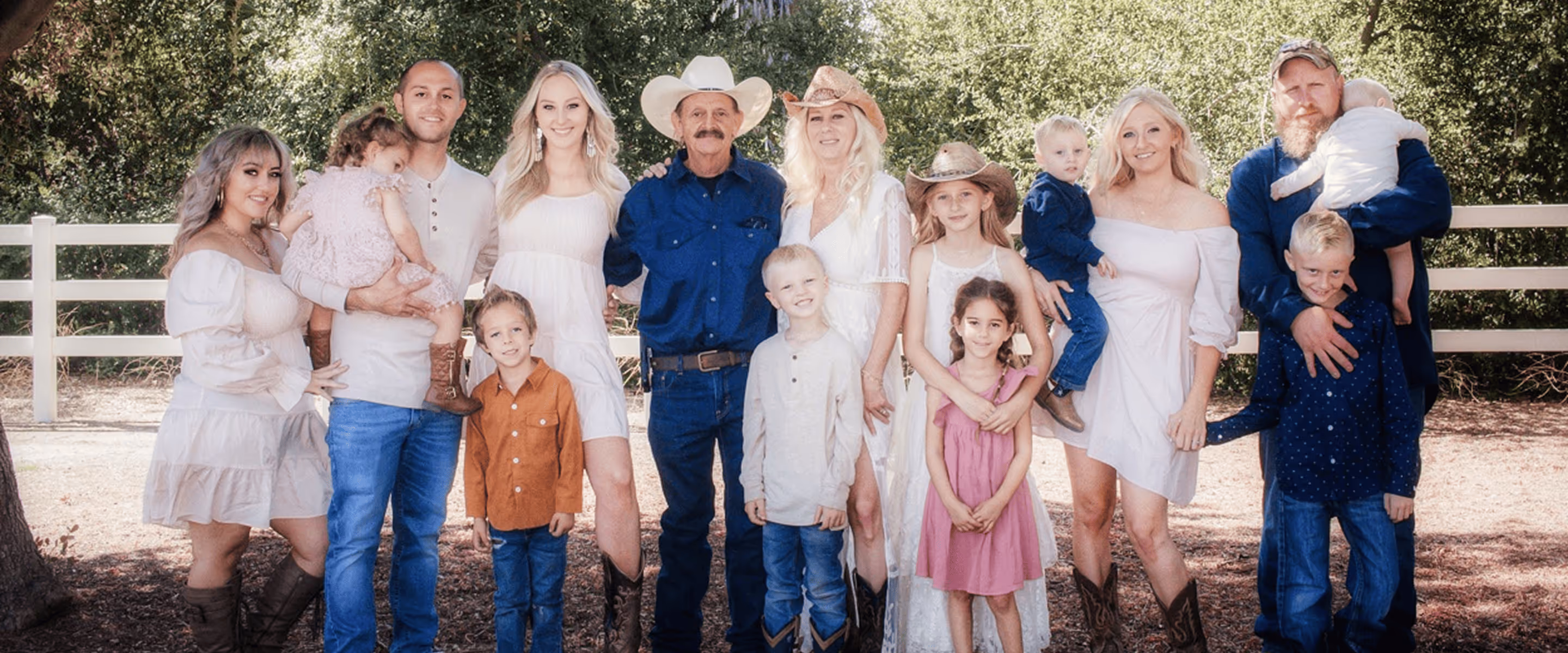 A group of adults and children posing together outdoors, wearing casual and Western-style clothing.