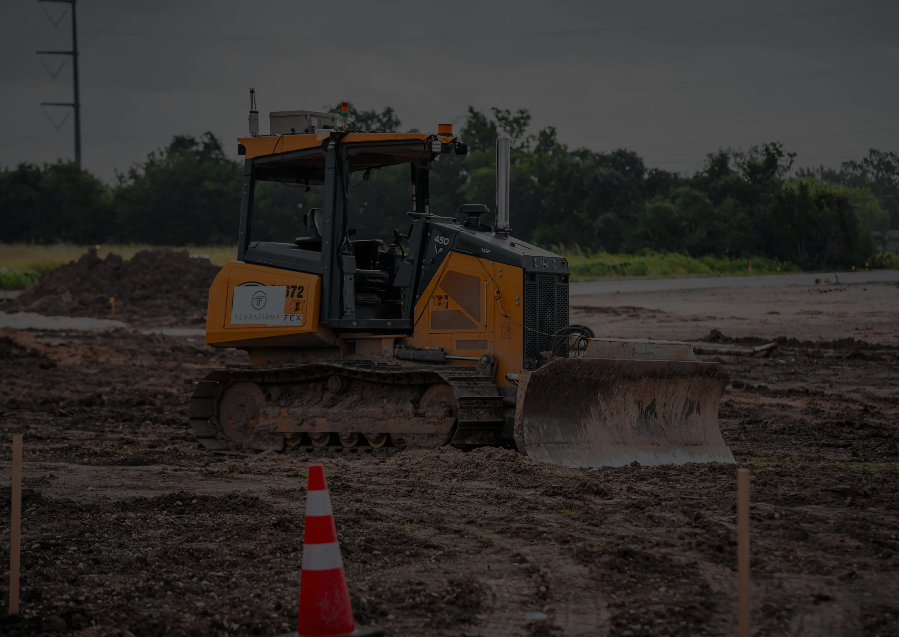 Bulldozer with TerraFirma logo working on a muddy construction site, with an orange safety cone in the foreground.