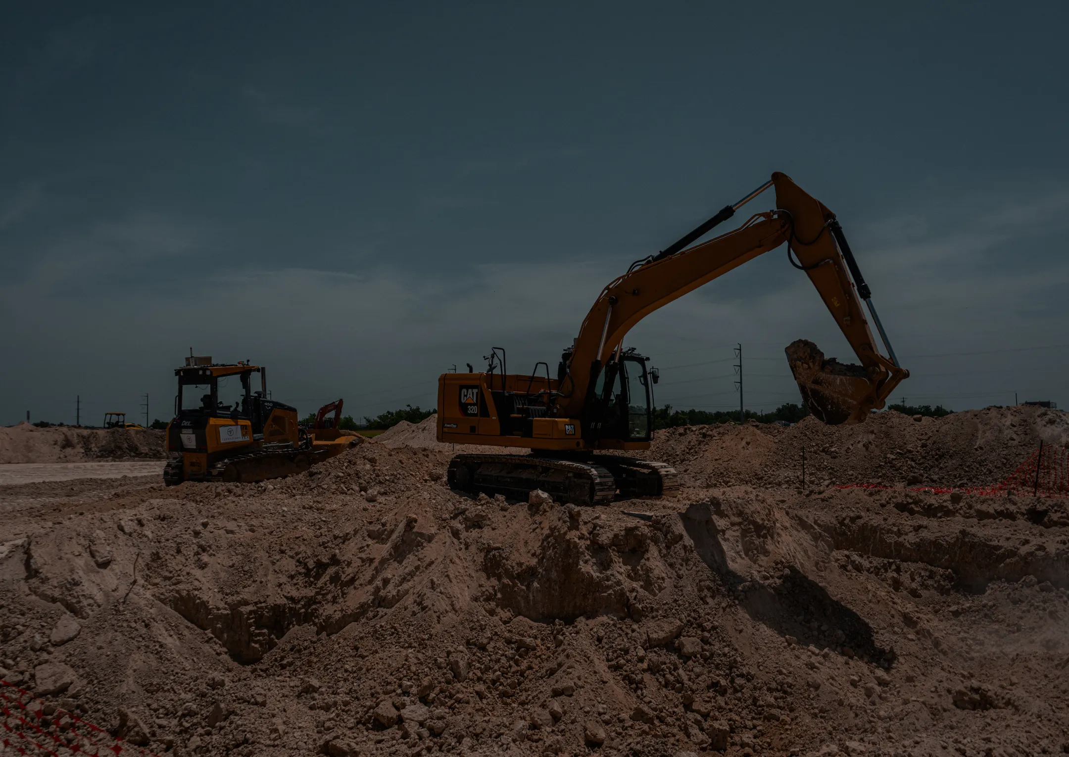 Construction machinery at a worksite: an excavator and bulldozer operating among soil mounds.
