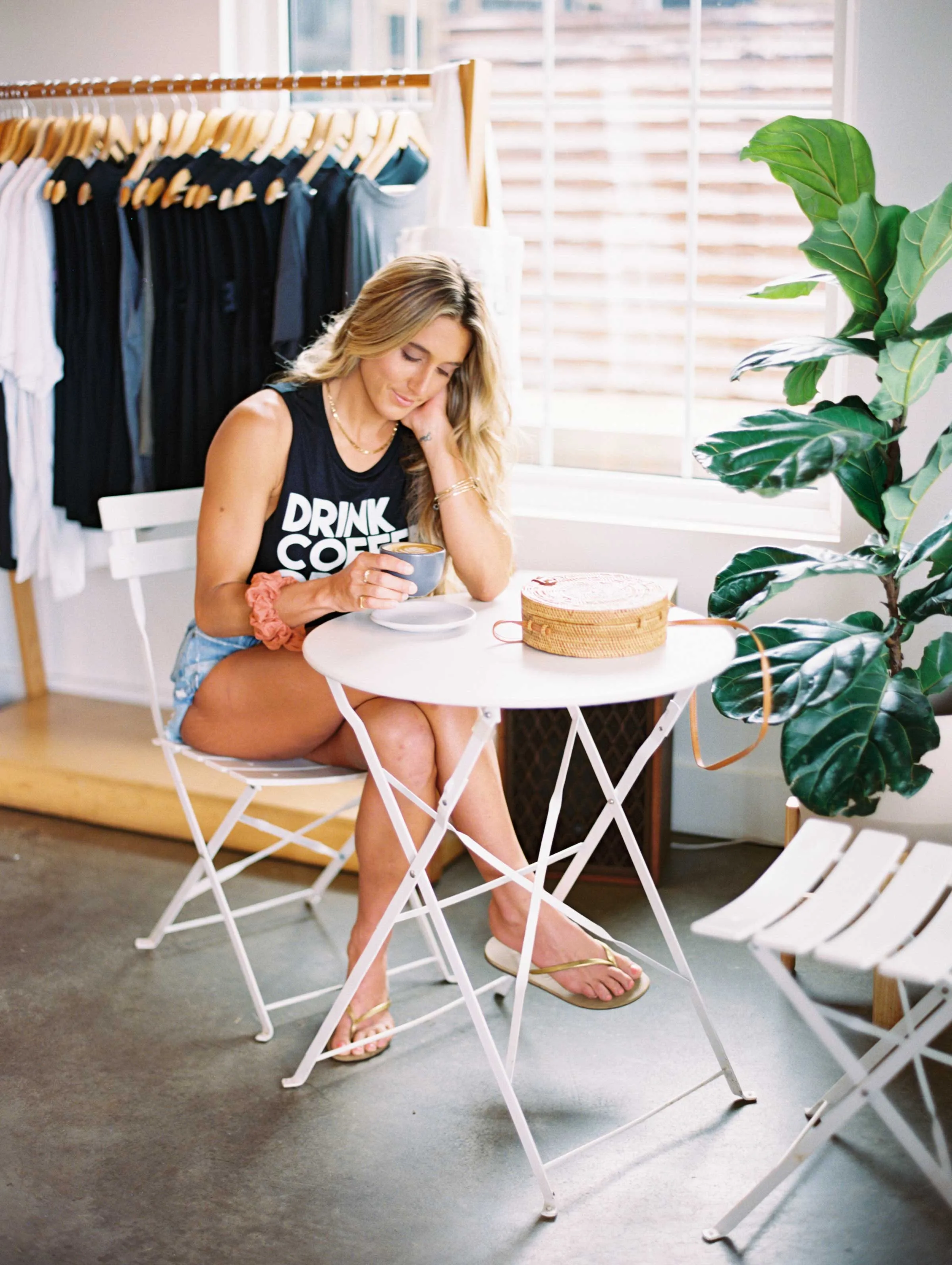 Woman in black tank top and shorts sitting at table with coffee cup in a bright room