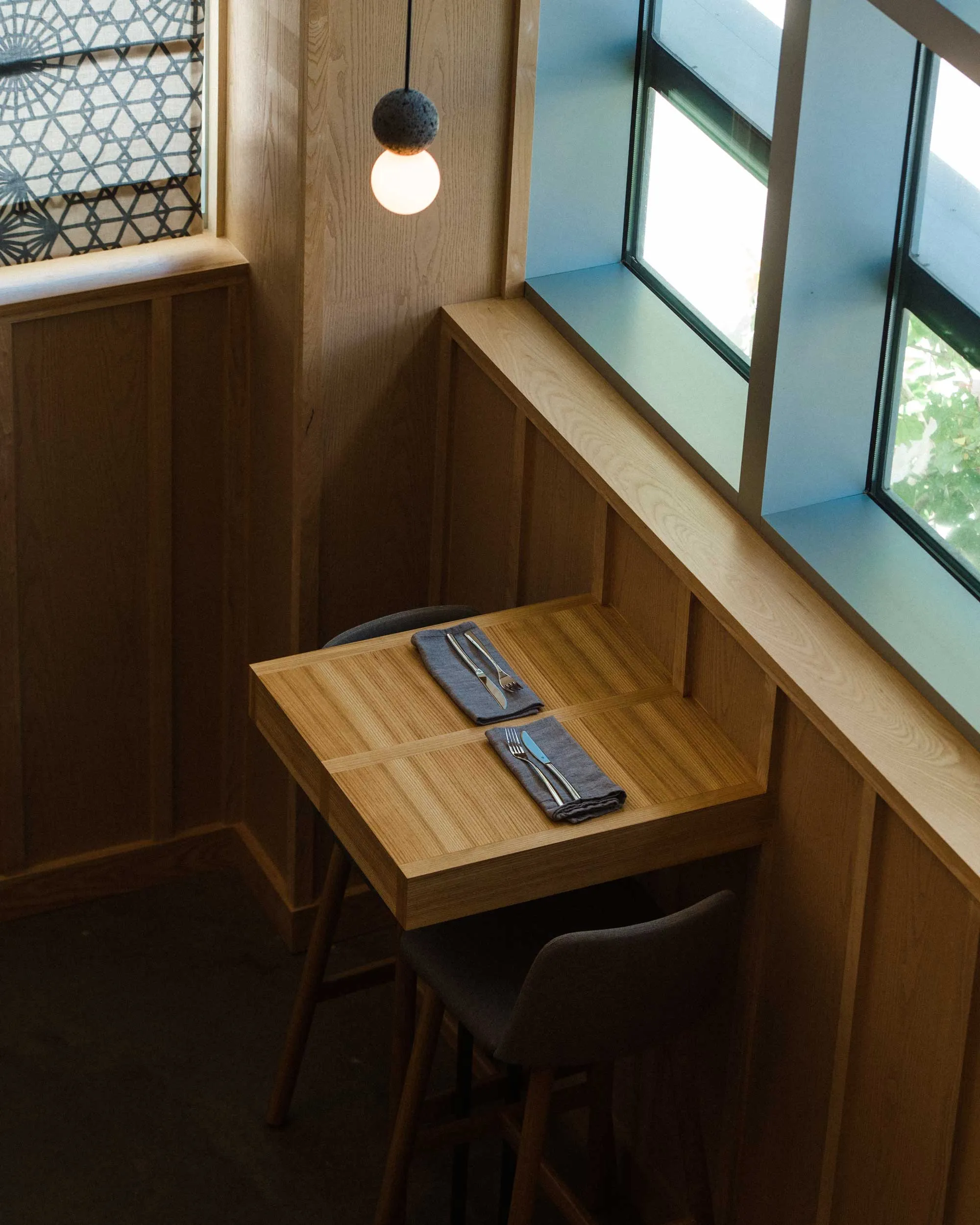Small wooden table with two place settings by a window in a cozy, minimalist dining space.
