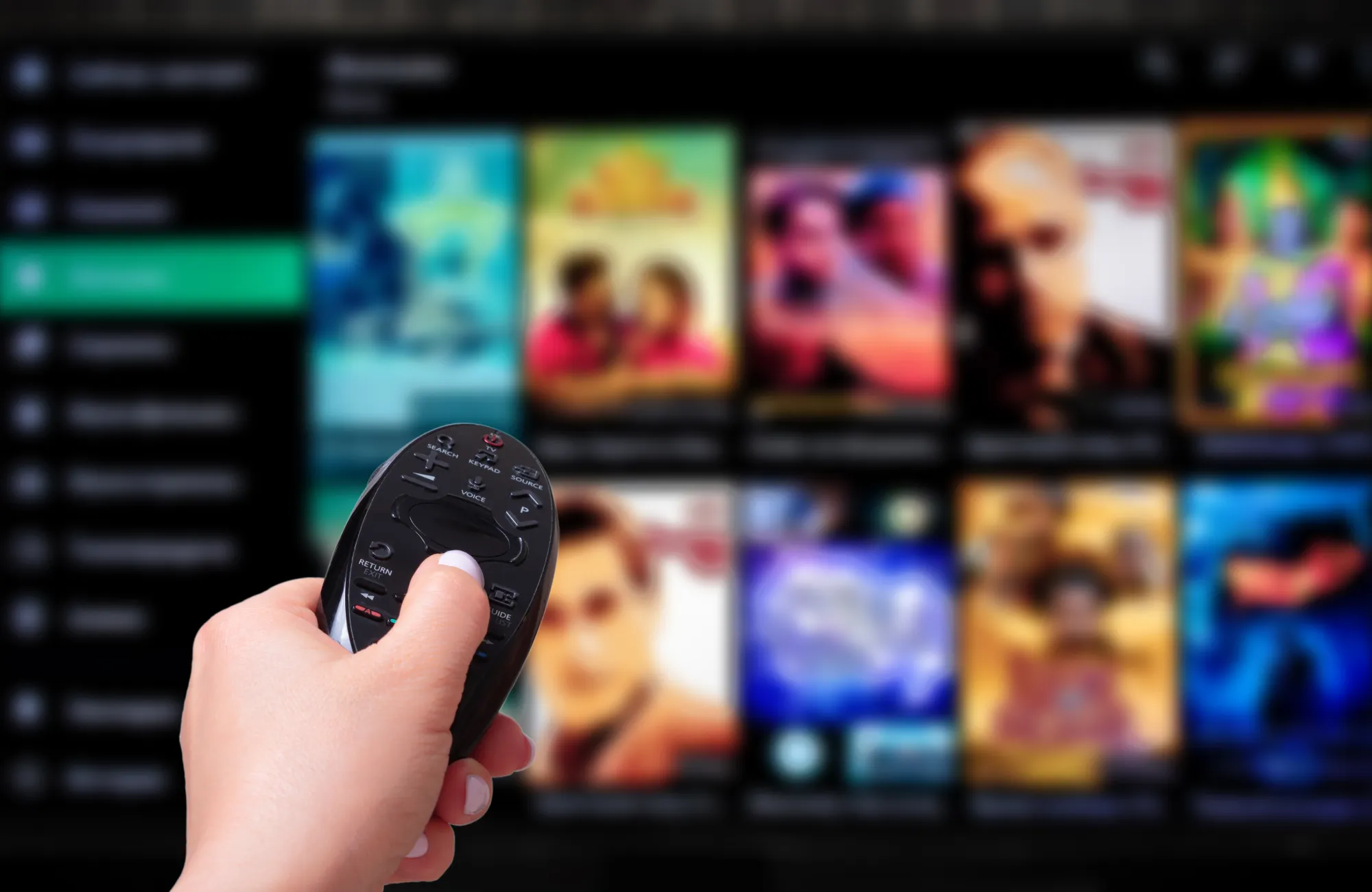 A hand holds a remote control, pointing at a TV screen displaying various movie covers.