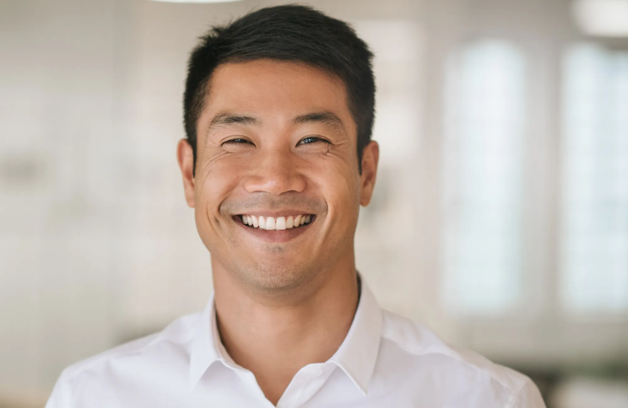 A person is smiling at the camera while wearing a white shirt.