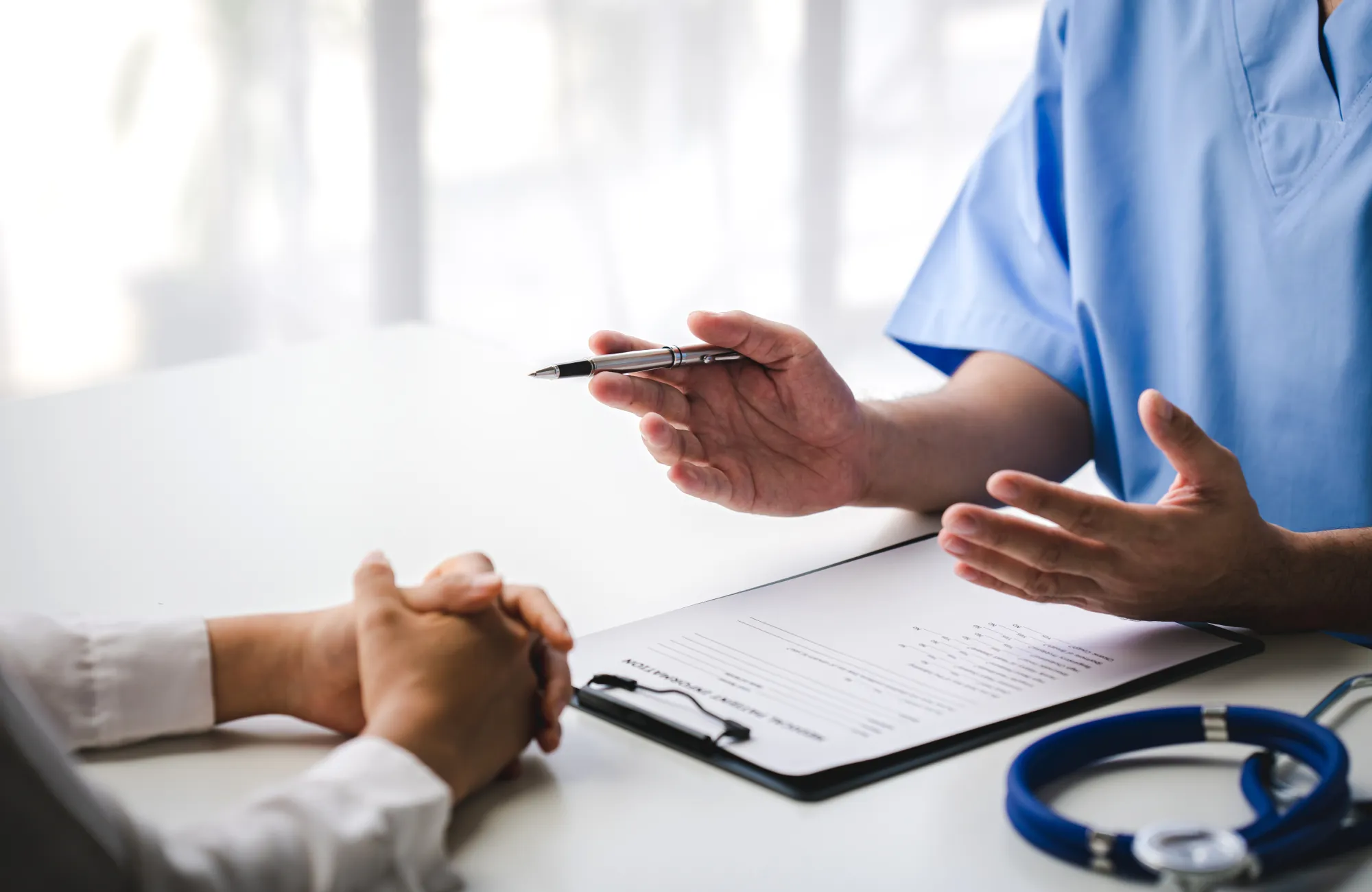 A doctor in a blue uniform explains a medical form to a patient at a table.