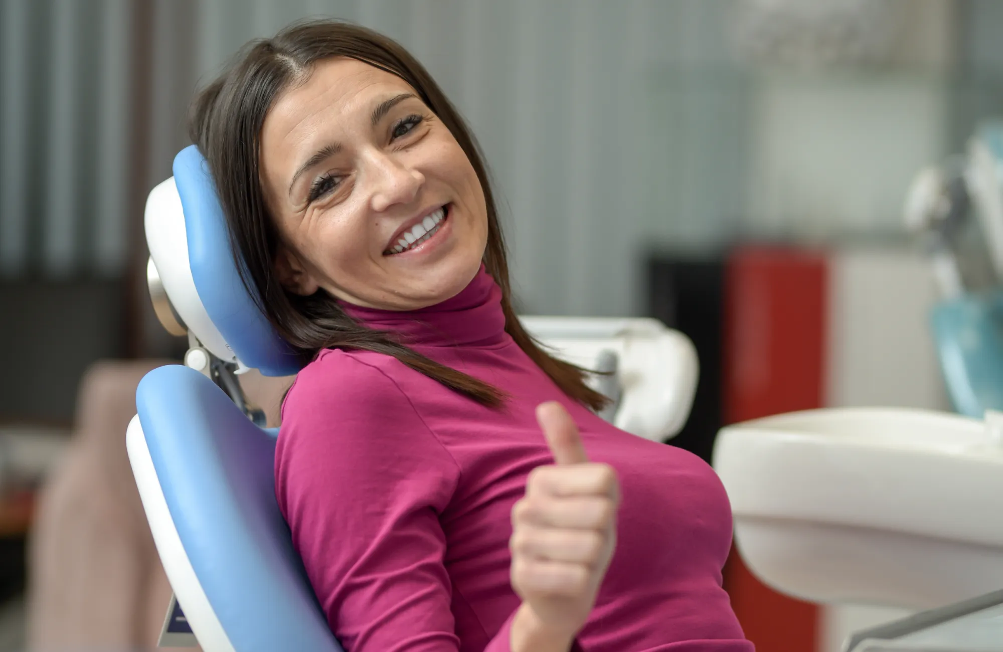A woman in a dental chair smiles and gives a thumbs up.