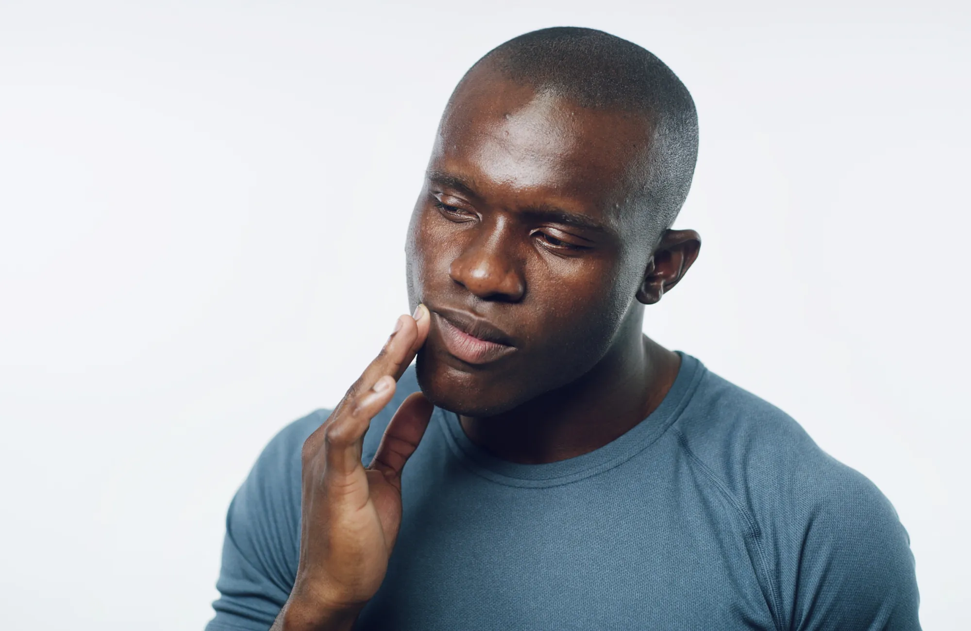 Man in a blue shirt touching his chin thoughtfully against a plain background.