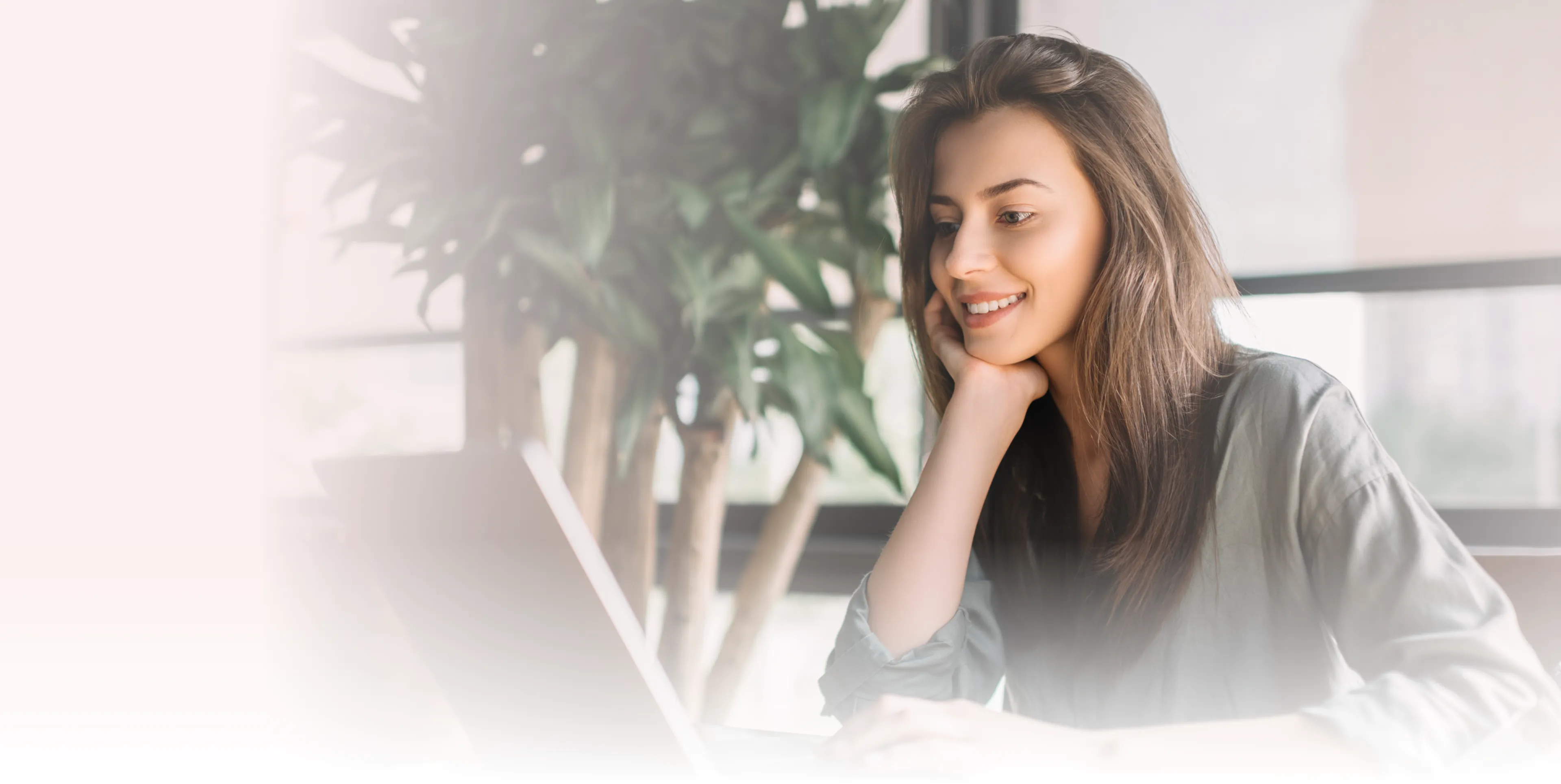A woman smiles while looking at a laptop screen indoors.