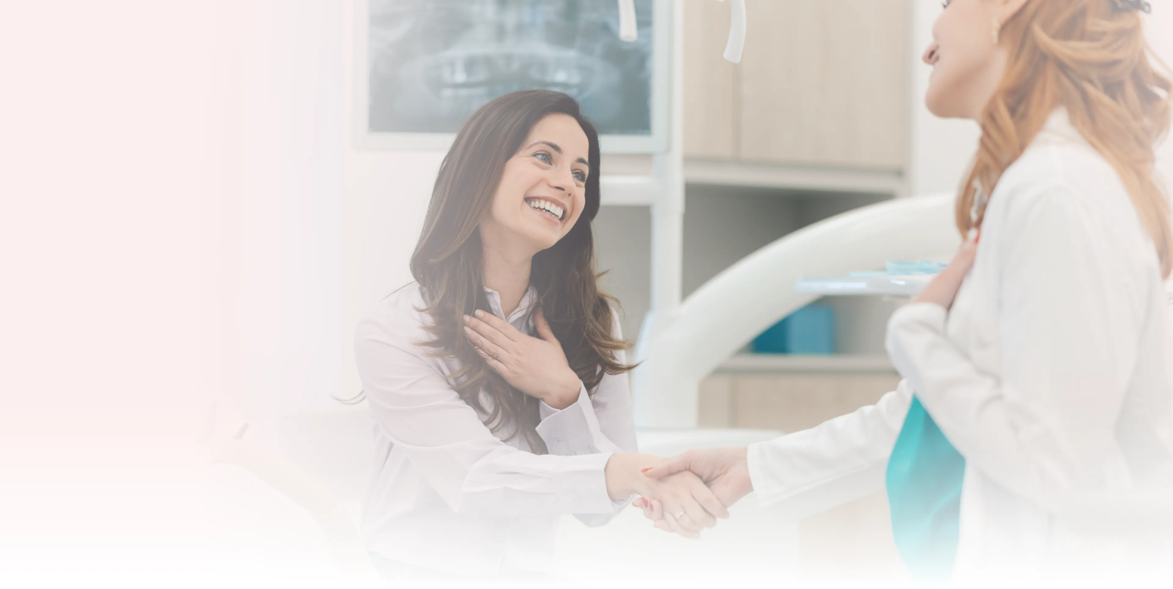 A smiling woman shakes hands with a dentist in an office.