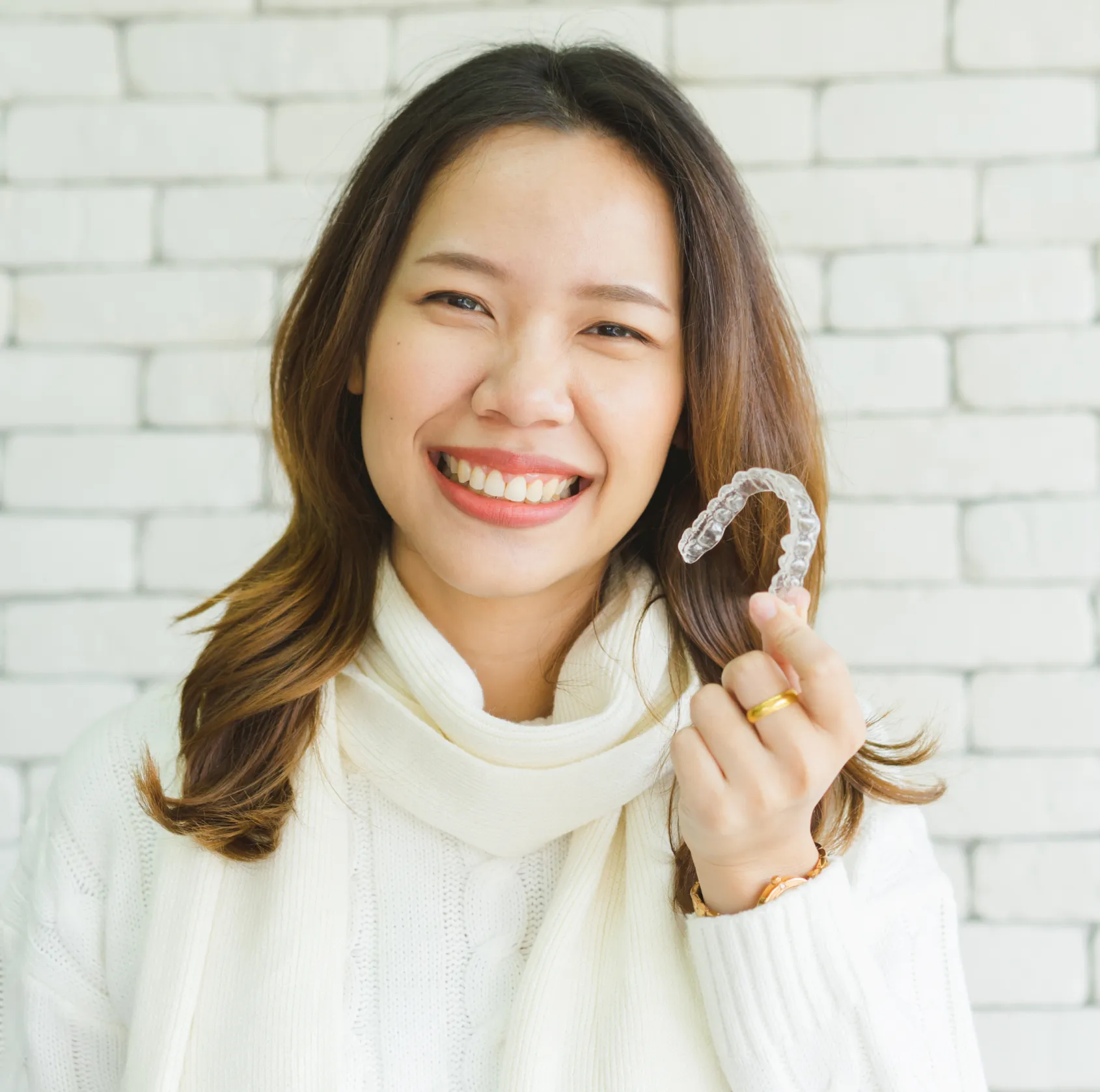A woman smiles and holds a clear dental aligner in her right hand.