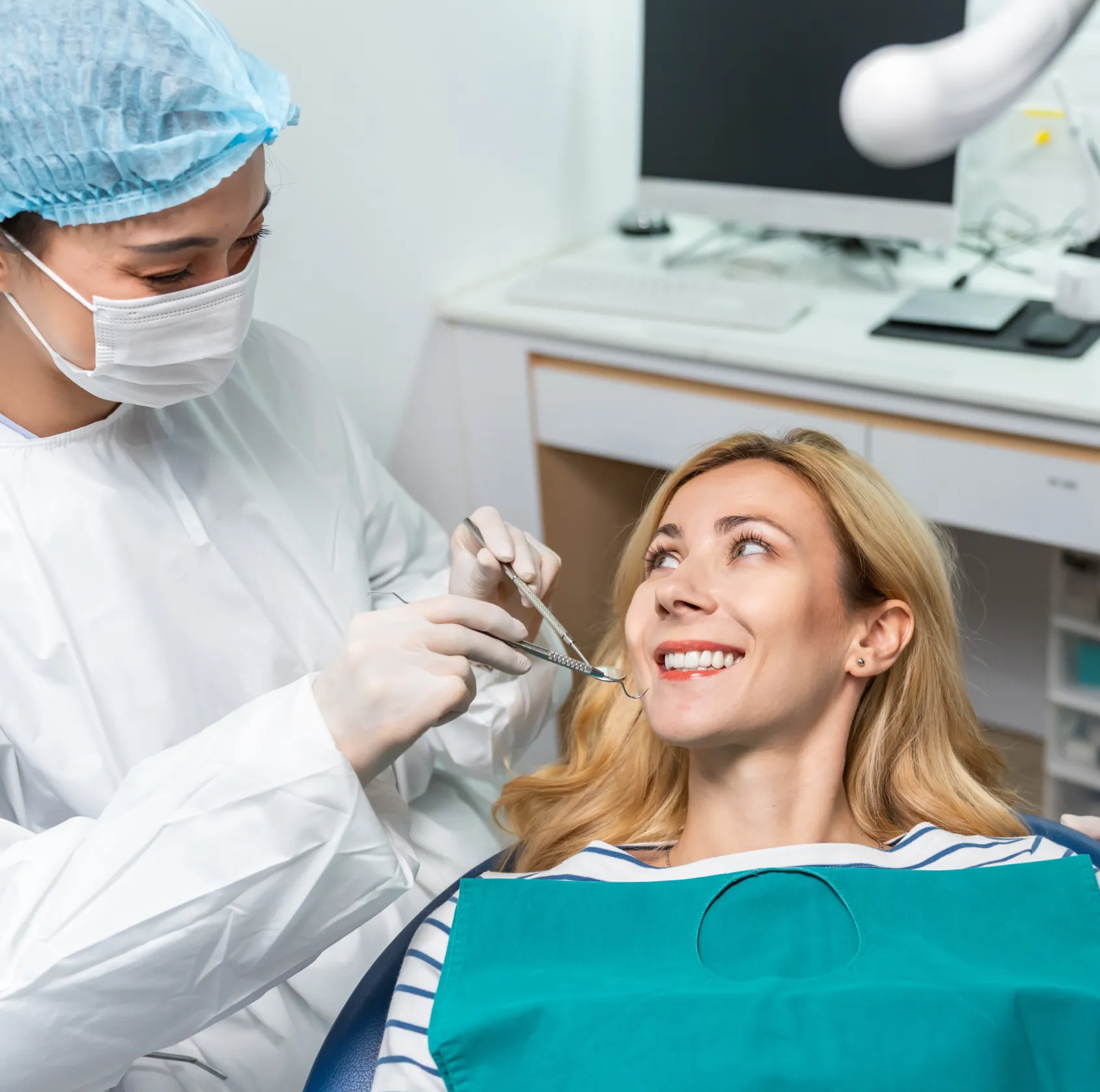 Dentist in white coat examines and talks to a smiling patient in a dental clinic.